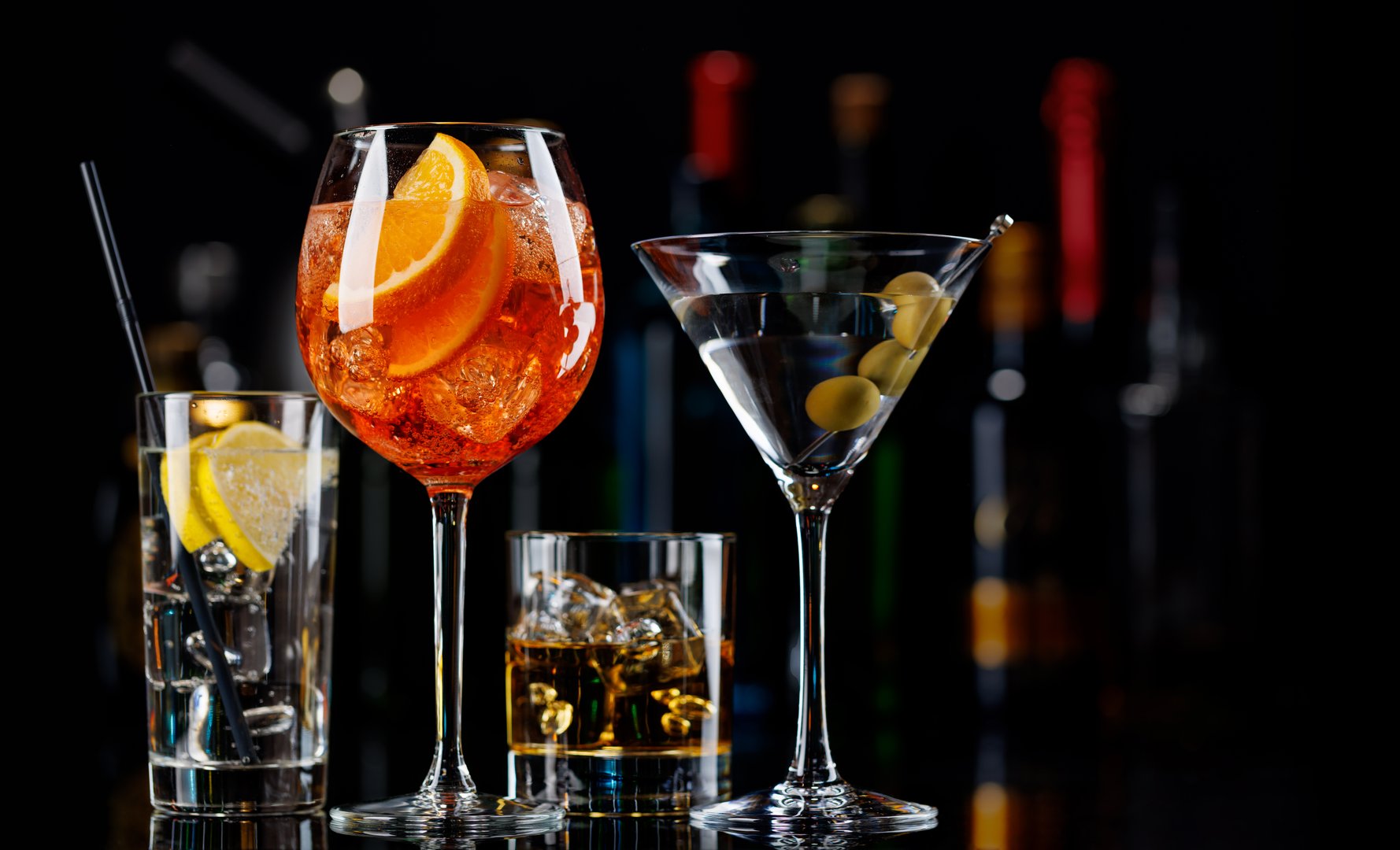 Various cocktails on a bar table. The colorful bokeh of illuminated bottles in the background enhances the mood, creating a dynamic and lively ambiance