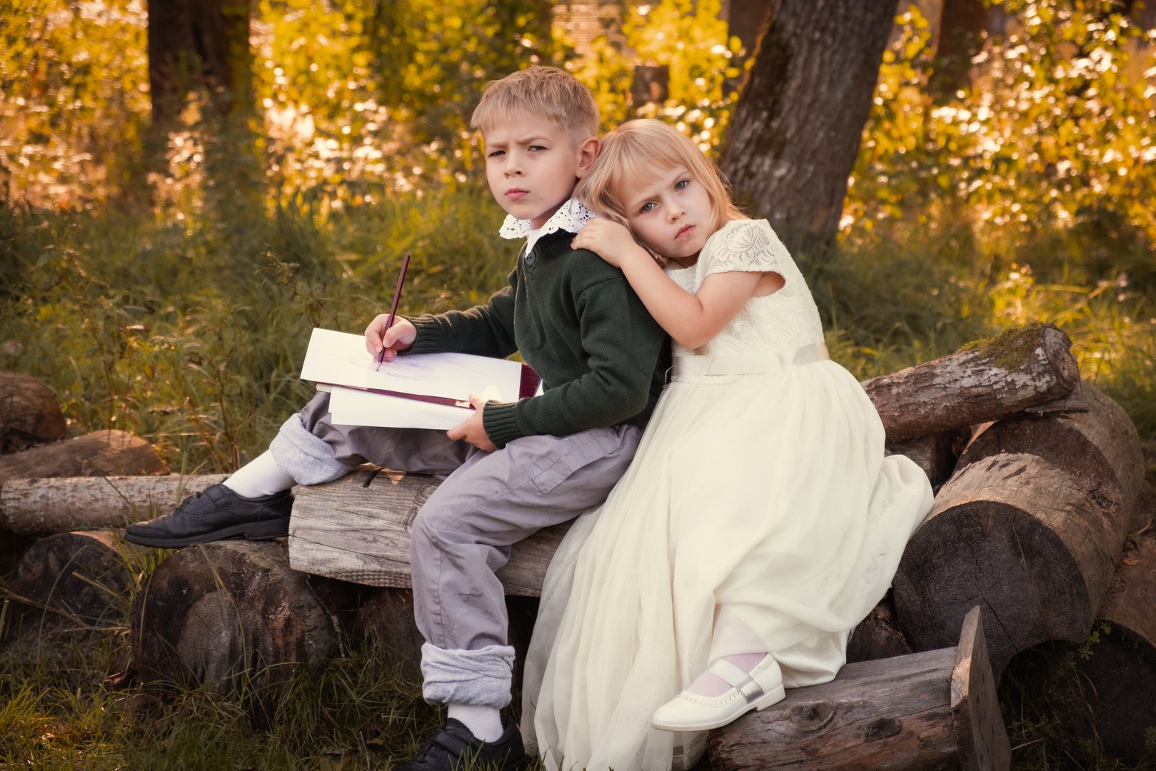 Two children embrace sitting on a log, showcasing their innocence in a beautiful outdoor setting. Charming Siblings, little boy and girl in Nature. Enchanting and Autumn Scene. Joyful Experiences