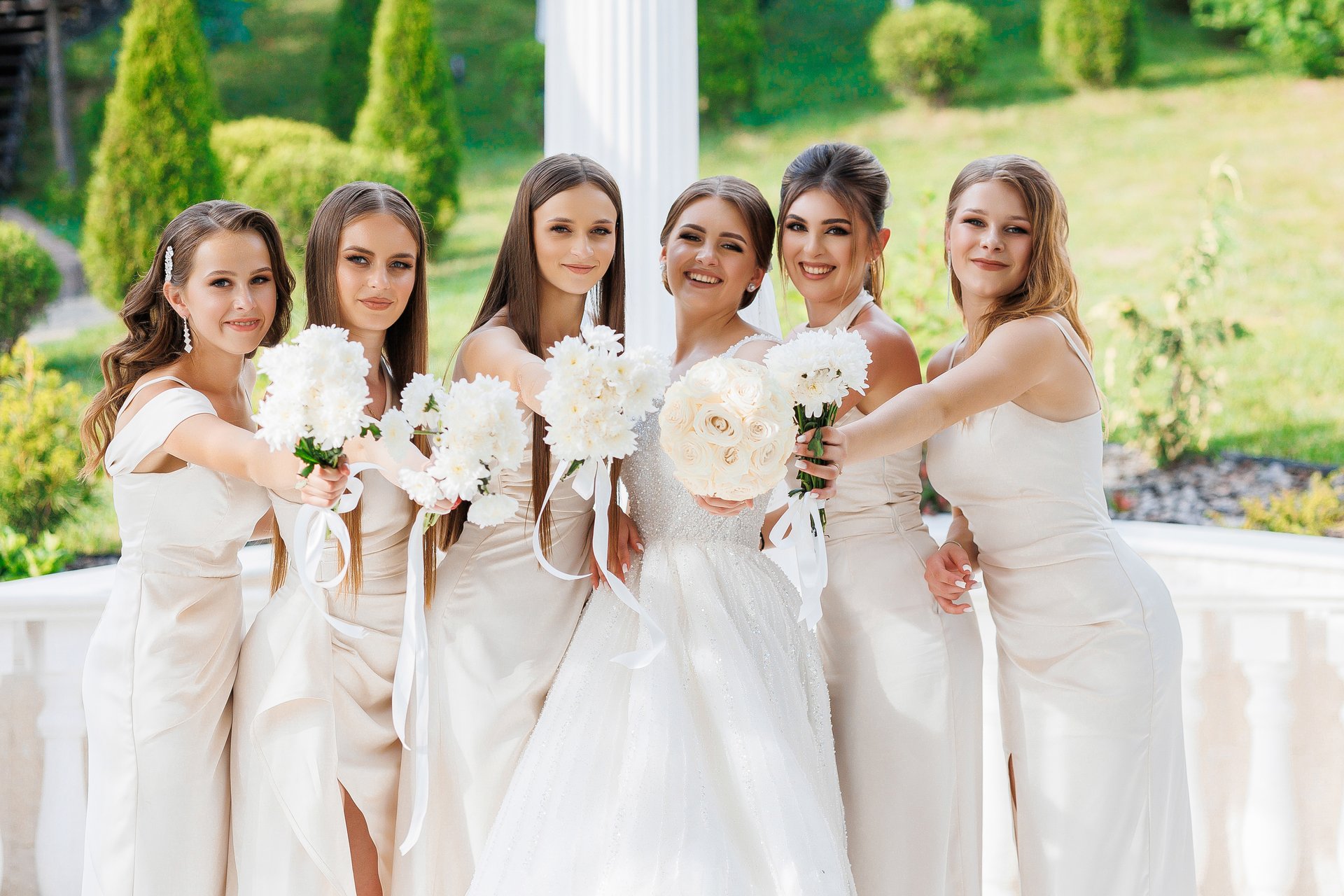 A group of women are posing for a picture, with one of them holding a bouquet of flowers. Scene is joyful and celebratory, as the women are likely attending a wedding or other special event