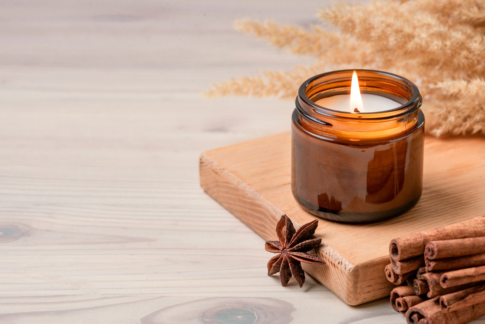 Massage scented burning candle in amber glass jar, winter hygge home interior decor on wooden table with cinnamon sticks and anise, copy space. Soy wax eco candle.