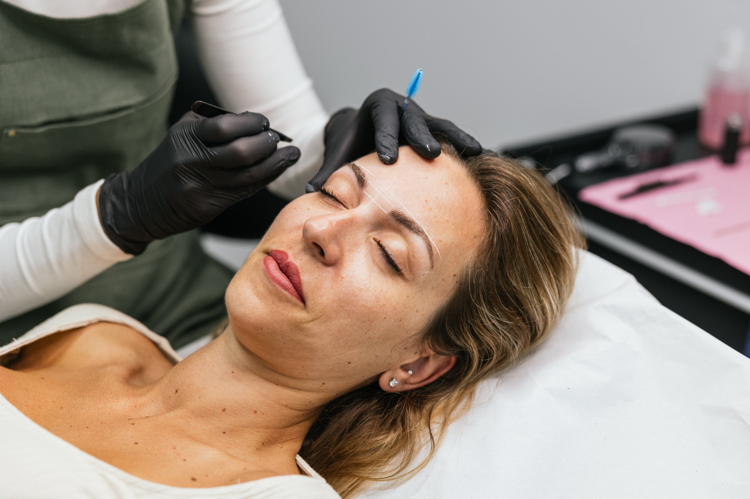 Beautician preparing eyebrows design on a young woman before microblading treatment in a beauty salon