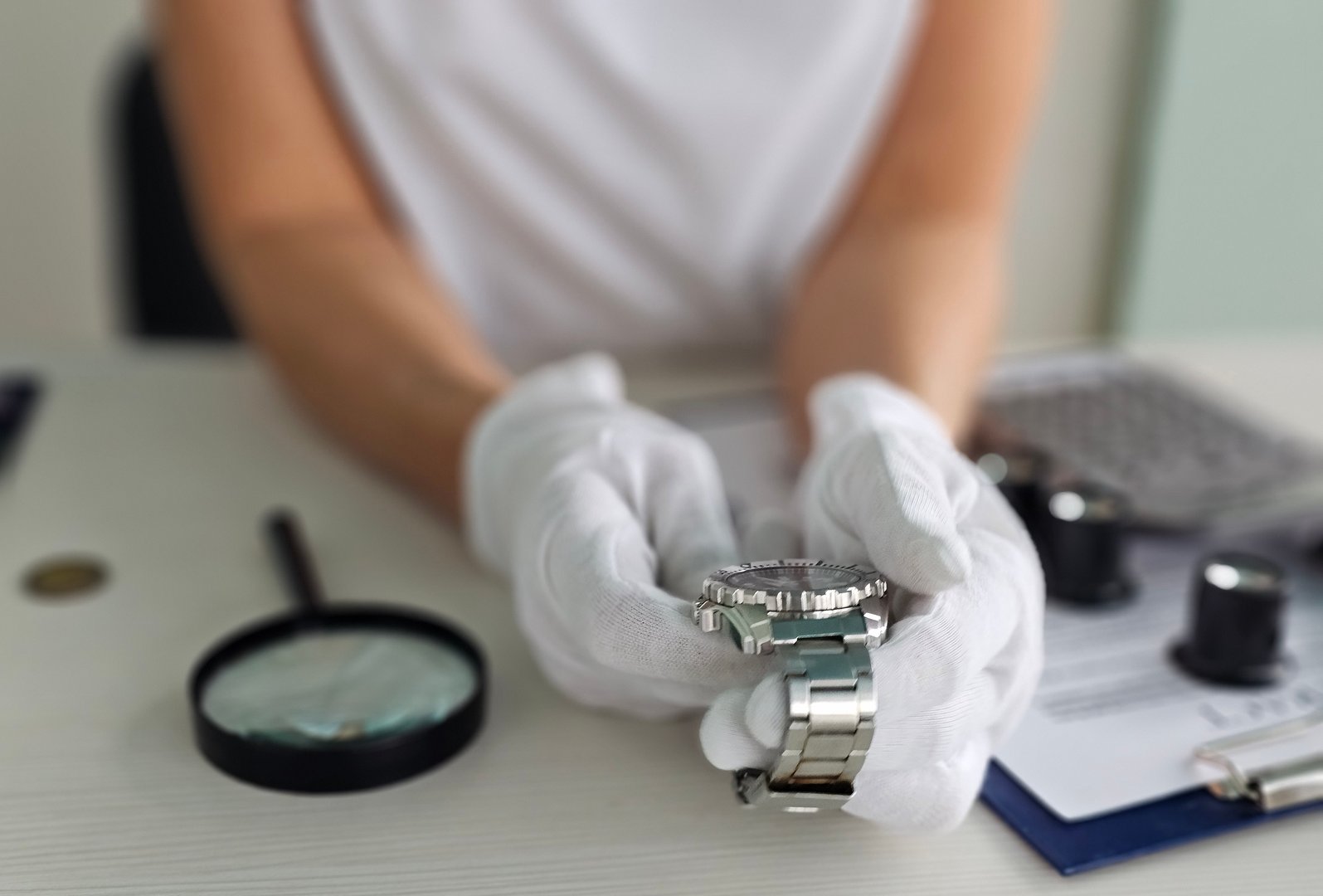 A watch repair specialist examines a luxury timepiece, wearing gloves for protection