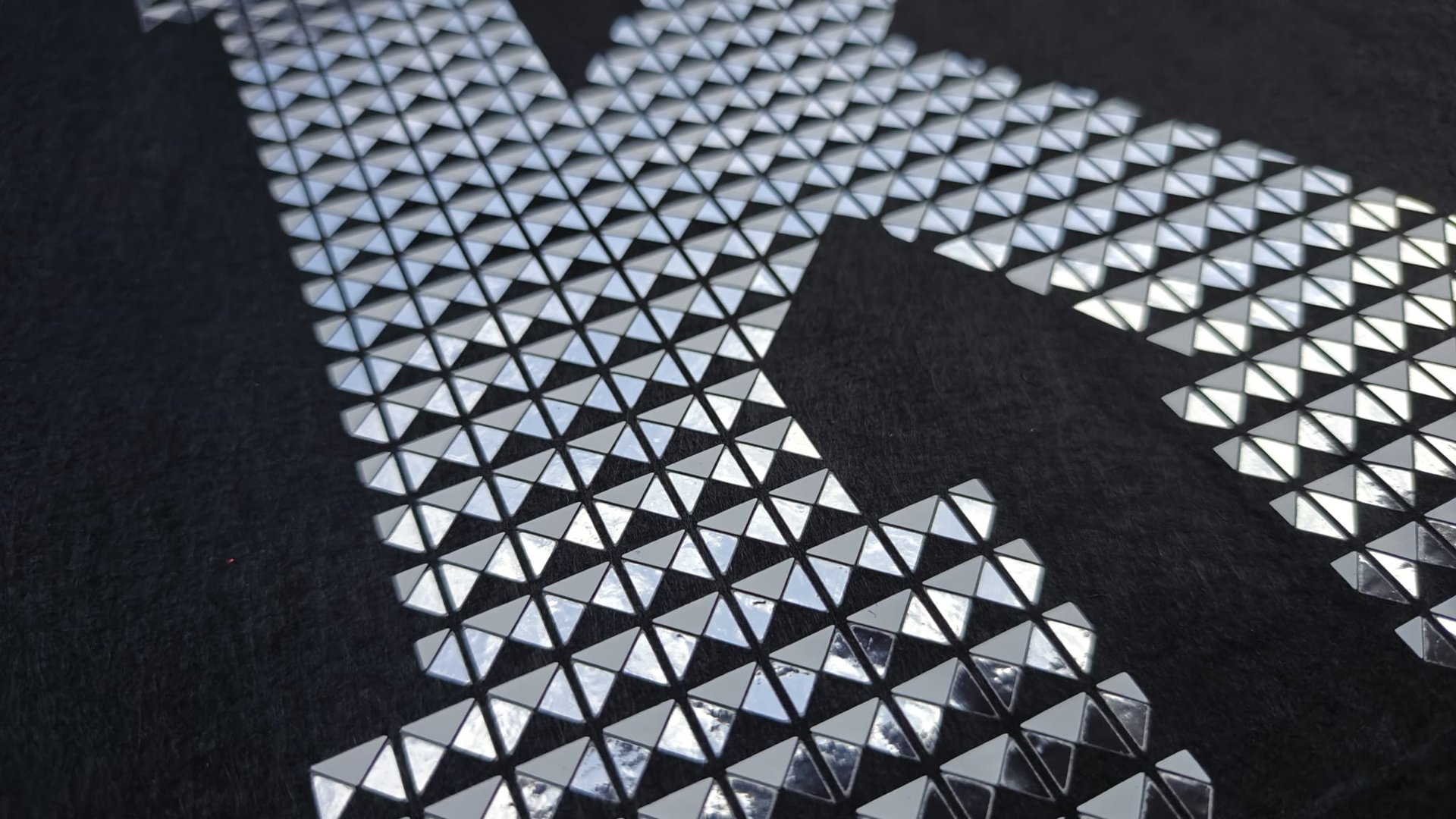 Close-up of a letter K pattern made from shiny metallic pyramid studs on a dark fabric background.