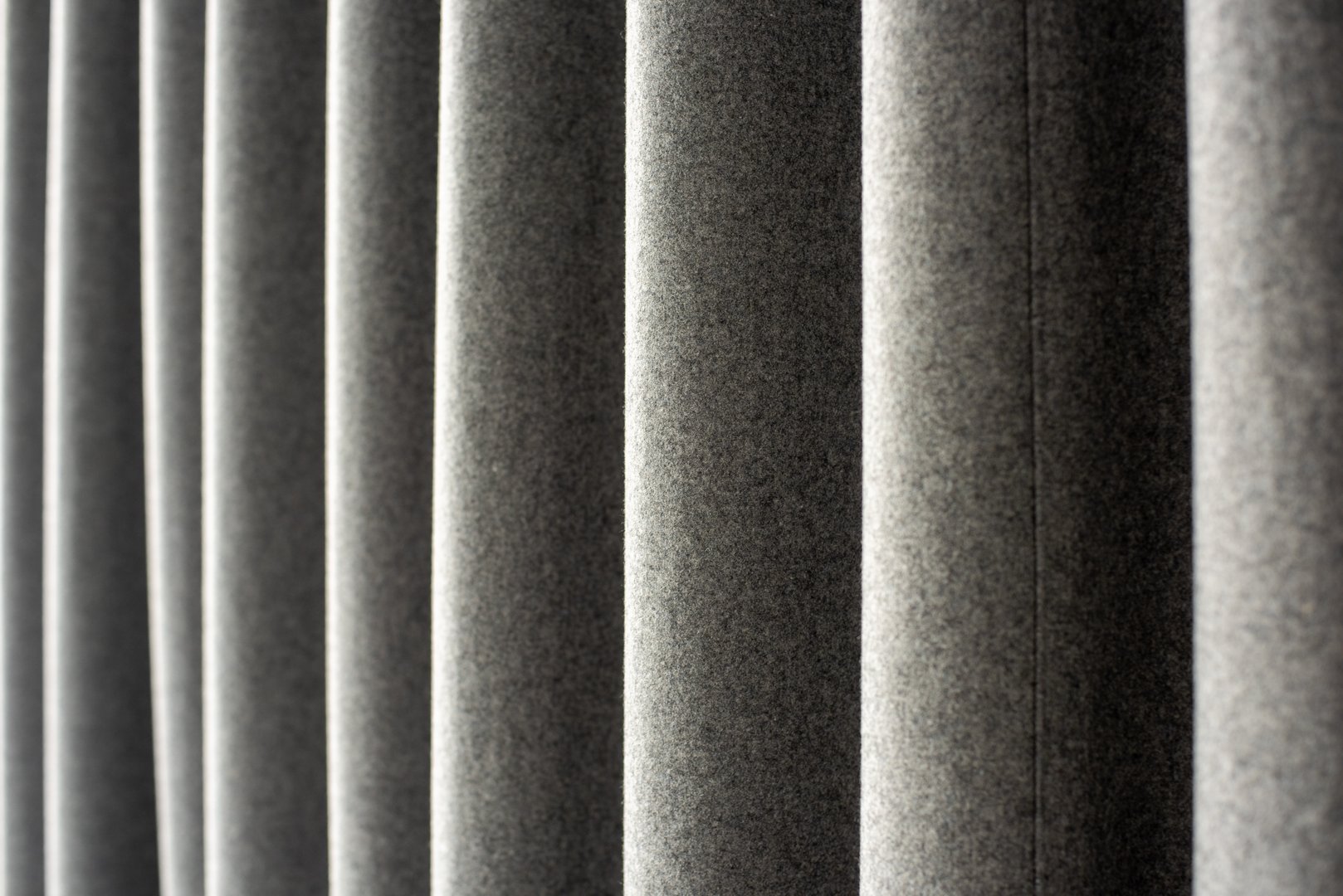 close-up view of vertically oriented, soft, grey fabric panels with a smooth, velvety texture. The panels are aligned in parallel, creating a rhythmic pattern of light and shadow across their surface