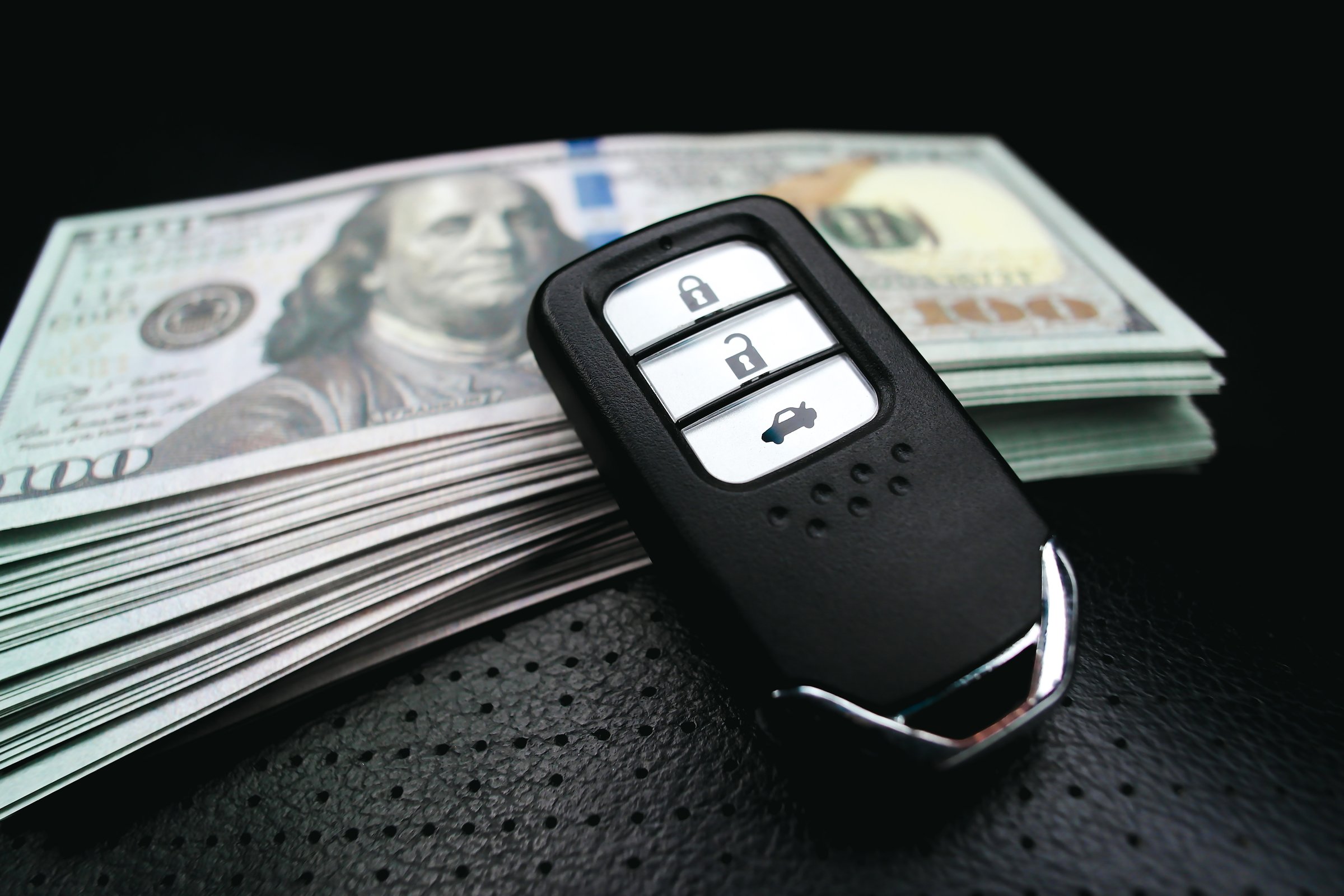 Car key or keyless remote and usd dollar banknotes on a black leather seat in a car. Buy sell and car loan concept