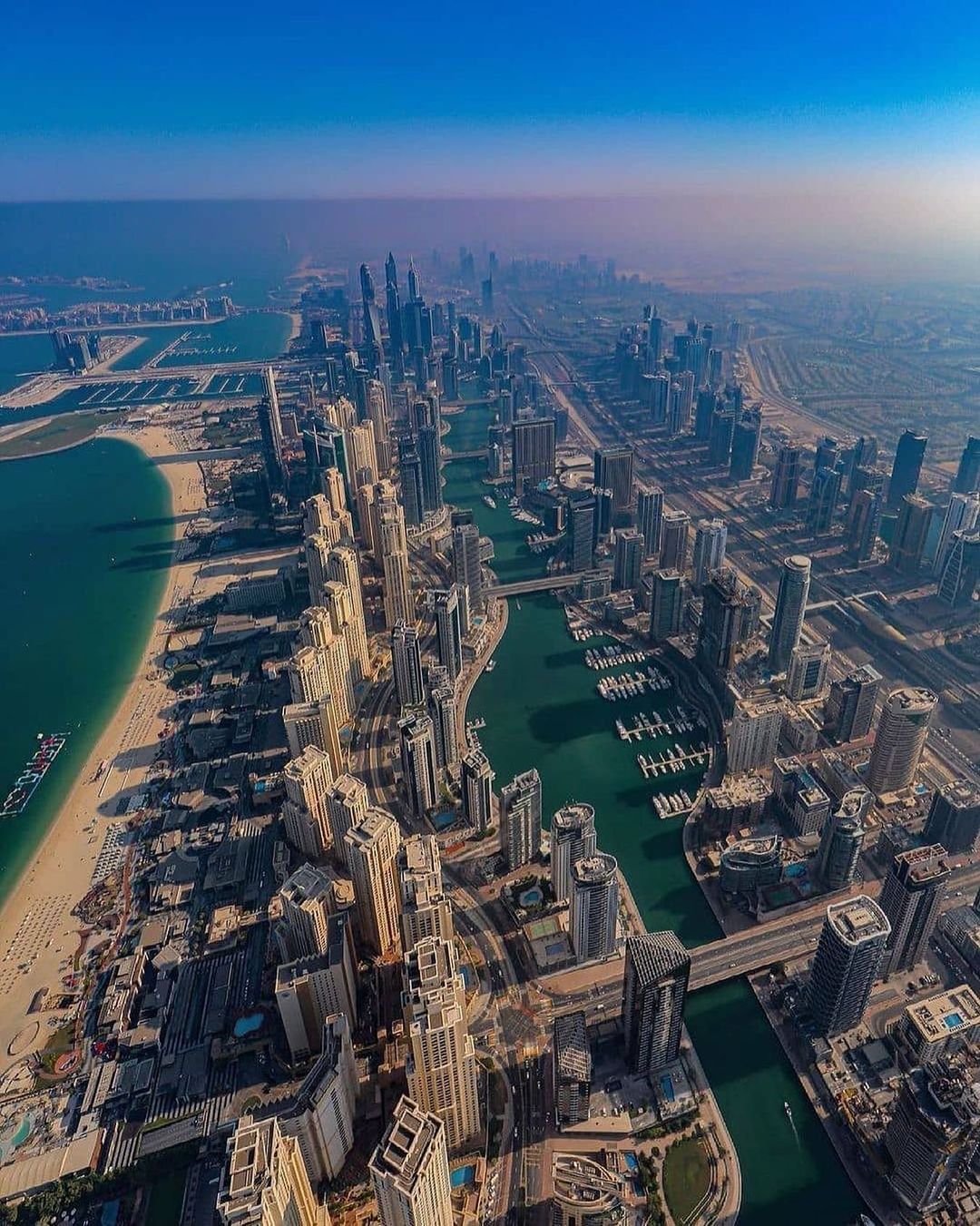 Aerial view of a coastal cityscape with skyscrapers, waterways, and a sandy beach, illustrating urban and natural elements.