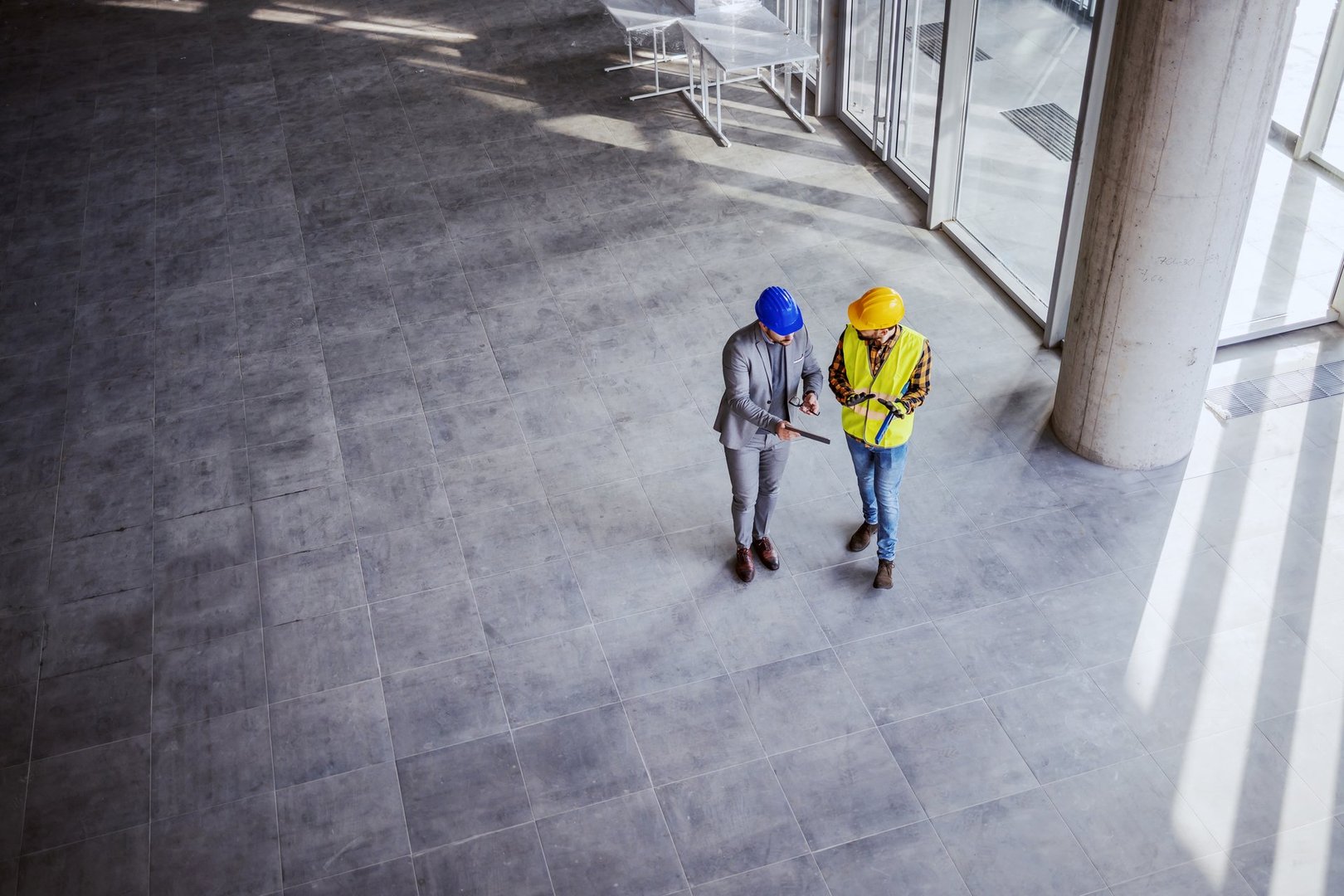 Top view of architect holding tablet and talking with construction worker about new ideas on project they working on. Building in construction process interior.