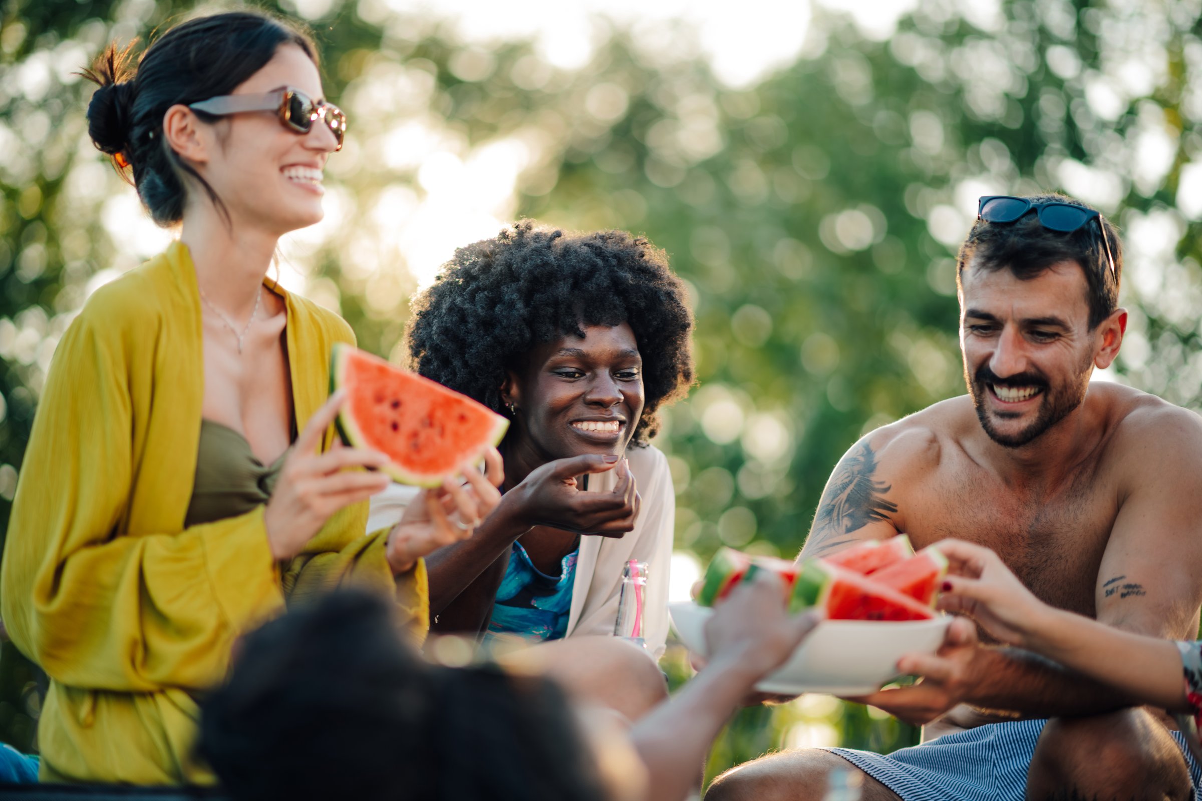 Cheerful multi-ethnic friends savoring juicy watermelon slices while enjoying a lively summer party outdoors in a vibrant garden setting