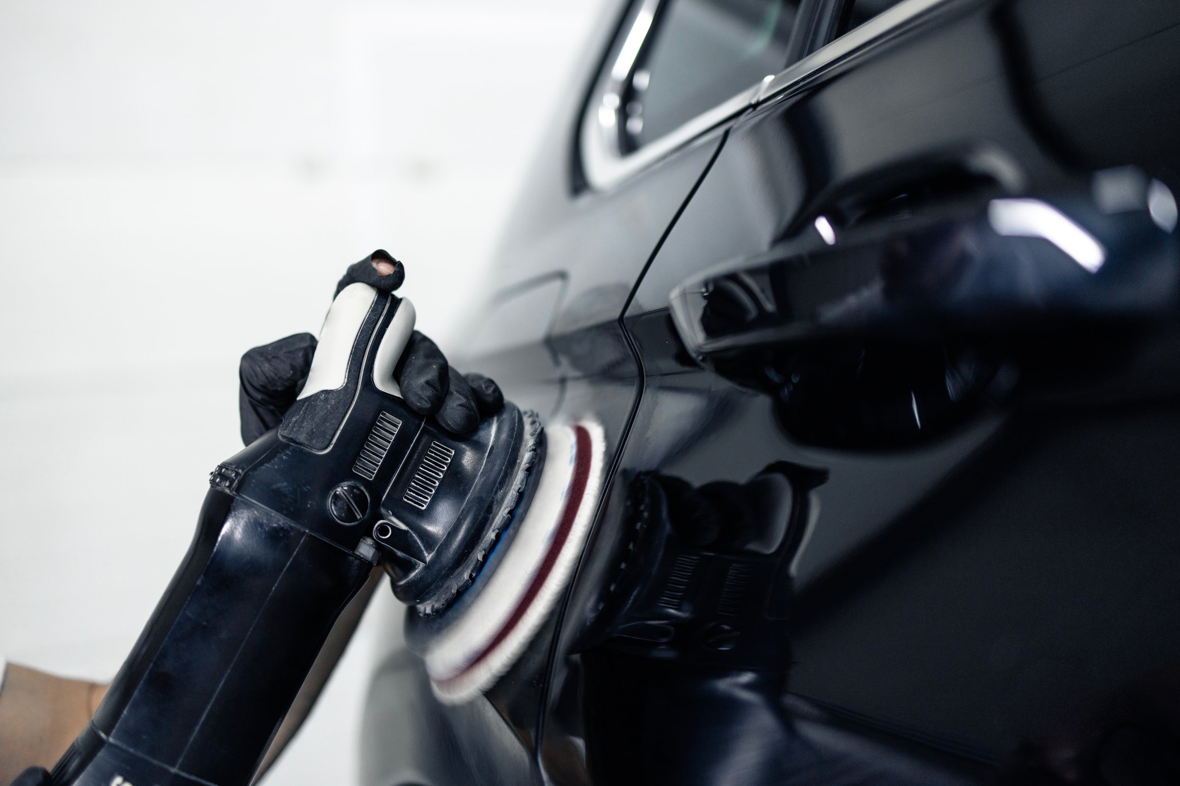 Close up view grinder machine polishing and waxing car in repair shop.