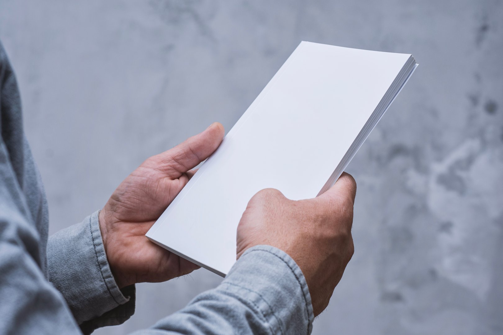 Realistic mockup of book cover, magazine in the hands of a man on concrete background. Concept for demonstrating editorial design, book covers and printed materials