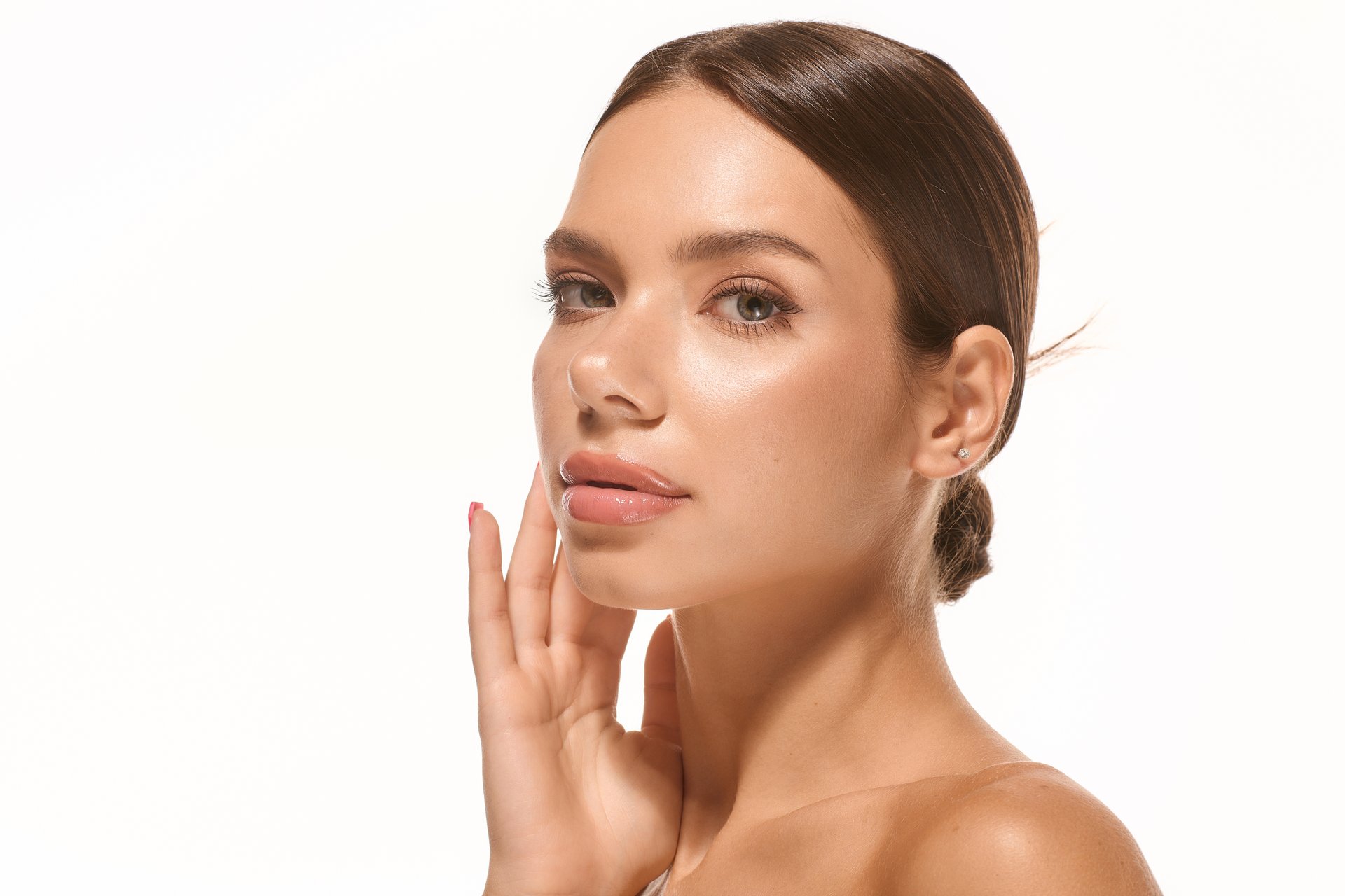 Young woman with radiant skin and subtle makeup poses gracefully against a bright backdrop.