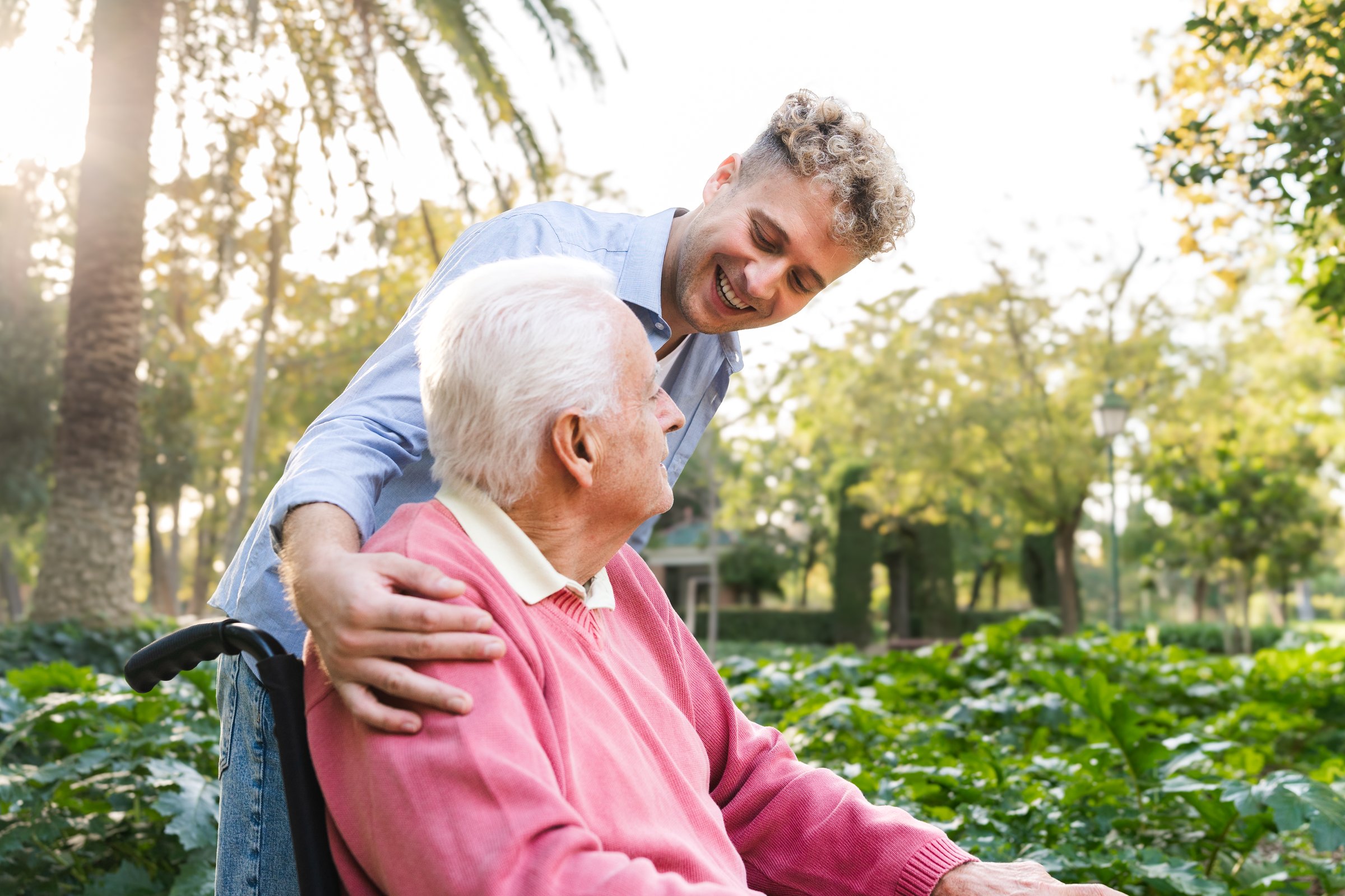 Close up of smiling grandson caring for senior man in wheelchair loving moment