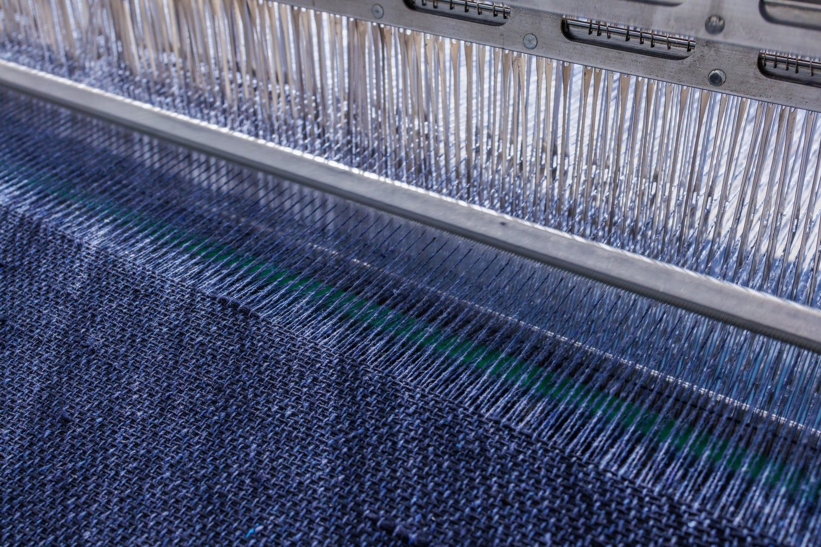 Detailed view of an automated weaving loom producing dark blue textile fabric with precision thread alignment.