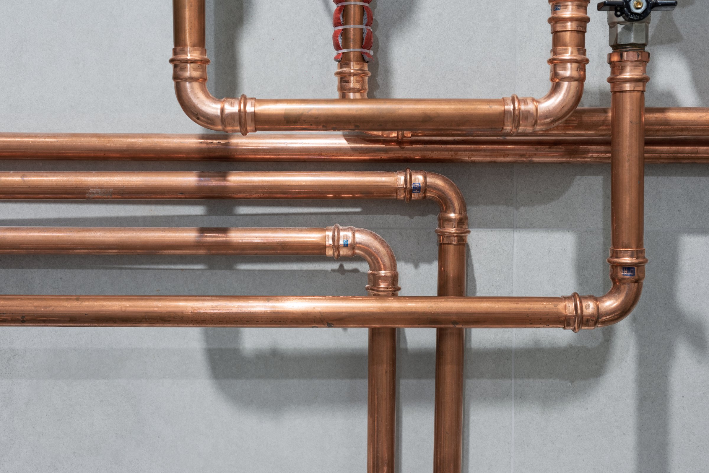 Cooper pipes connected with pressed or crimped fittings create an industrial pattern on grey tiled wall background