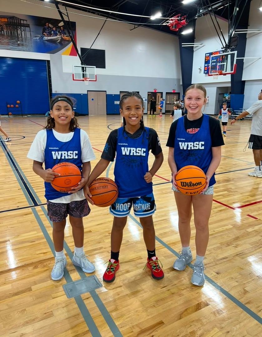 Three young basketball players holding basketballs, wearing WRSC jerseys, smiling on an indoor court.