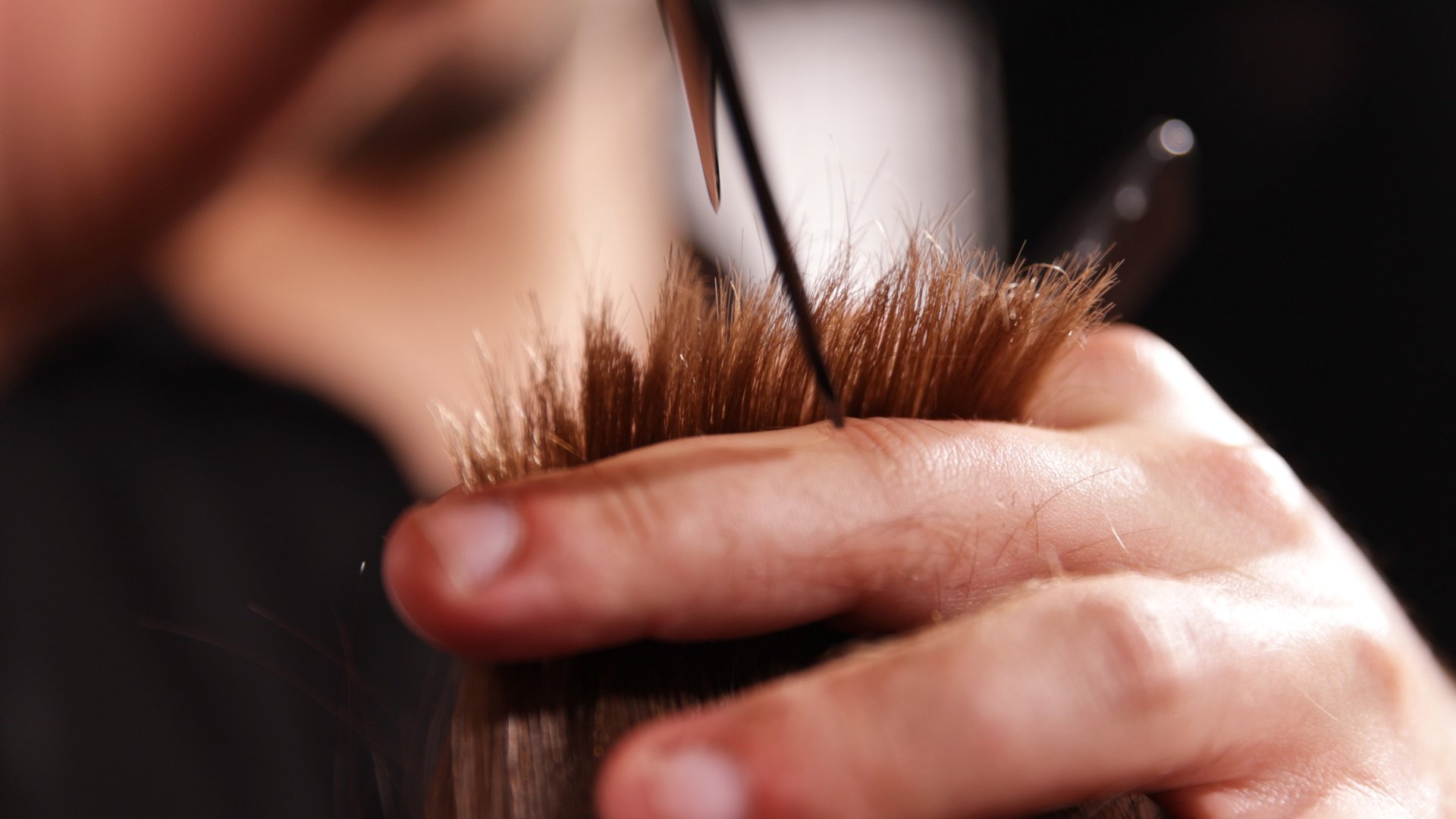 Young Man with Beard at Barber Shop. Barber is Preparing his Haircut. Dark Atmosphere, Black Background. Concept of Barber and a Client.