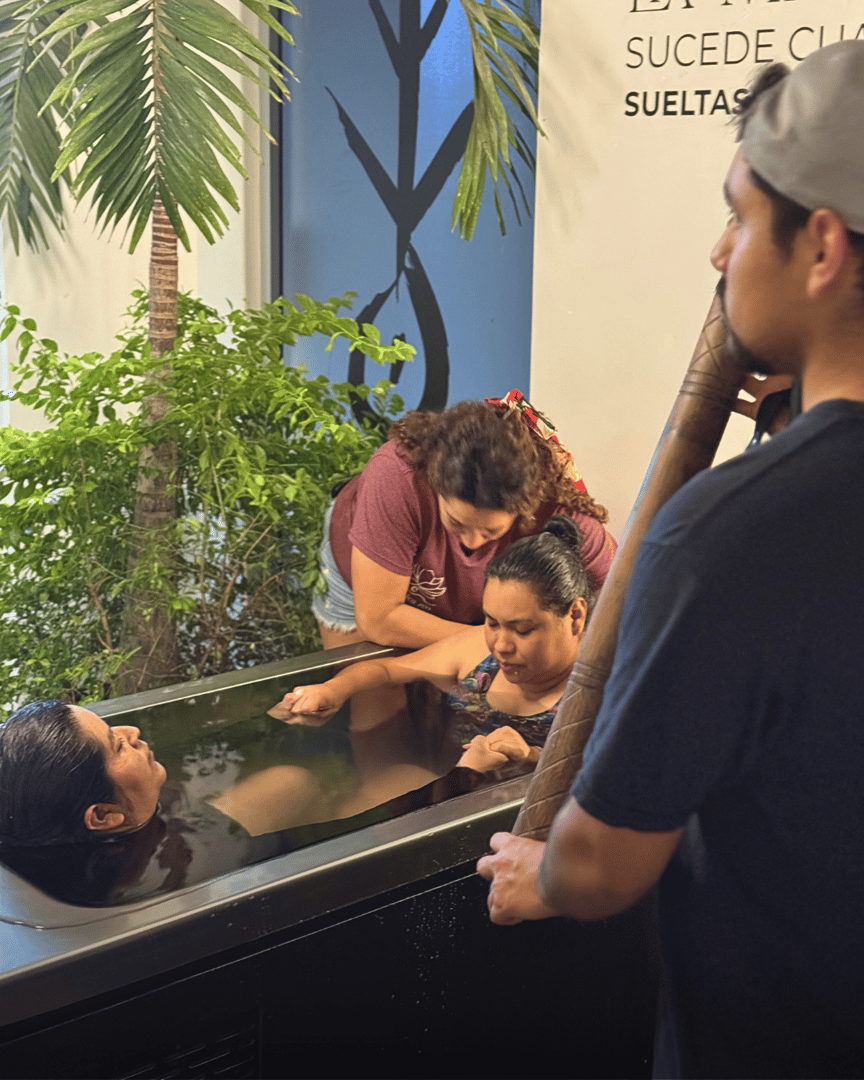People participate in a sensory experience involving water immersion, guided by an instructor in a tropical setting.