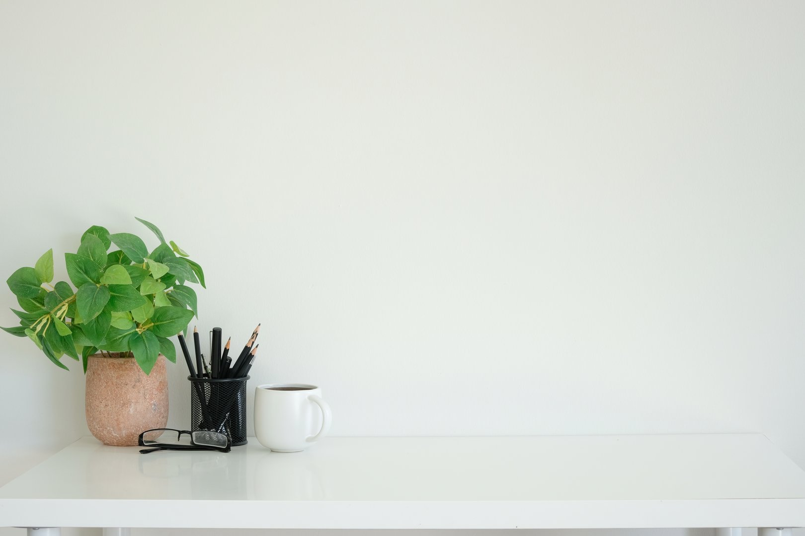 Minimalist workspace with a coffee cup, potted plant and pencil holder. Copy space for your text.