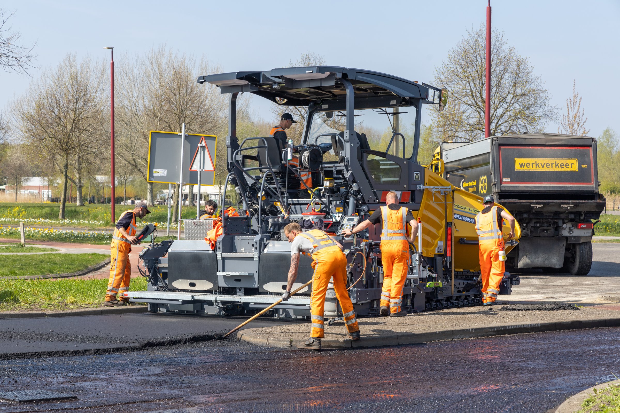 Road construction workers operate heavy machinery to lay fresh asphalt on a sunny day, improving road infrastructure in a rural area. Utrecht, Netherlands, 11 April 2025.