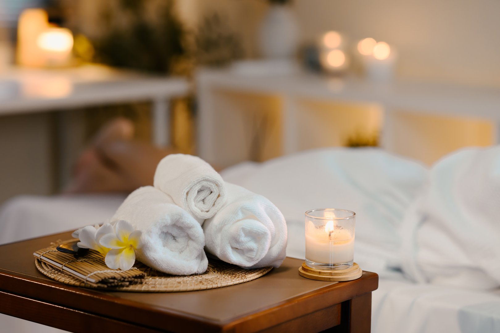 Rolled white towels, candle, and flower set the mood in a tranquil spa room.