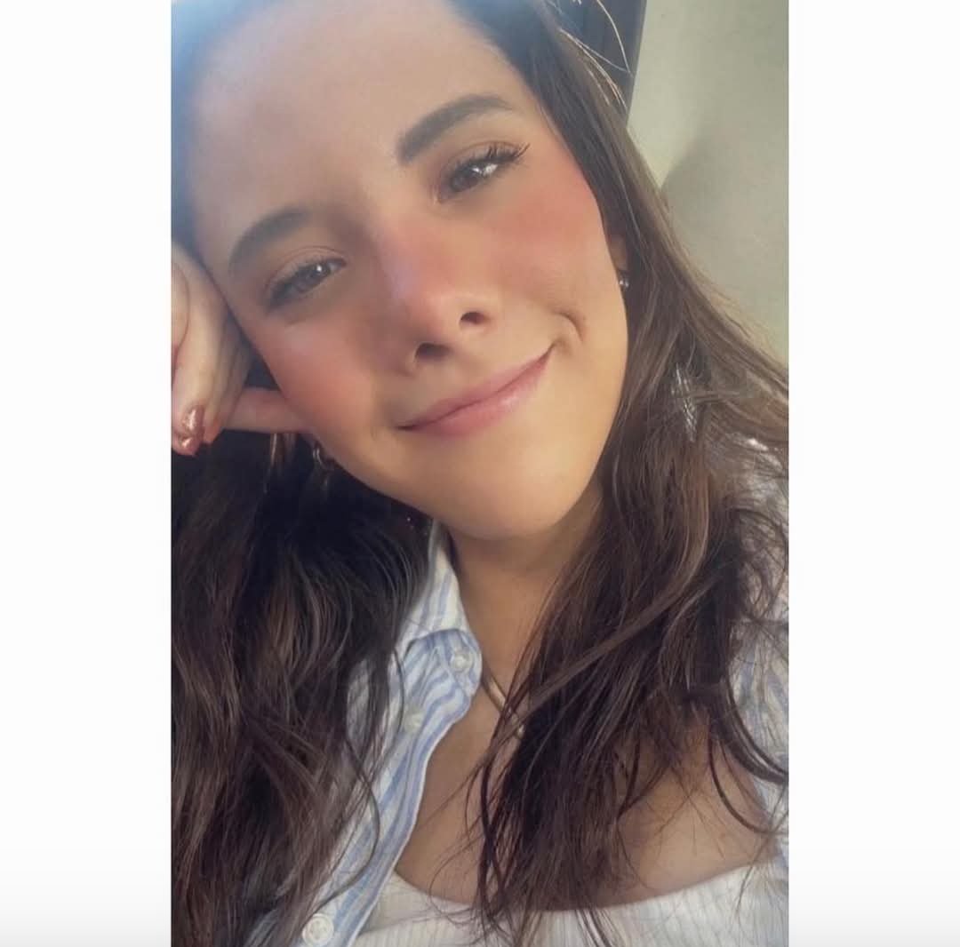 Smiling woman with long brown hair, wearing a striped shirt, rests her head on her hand.