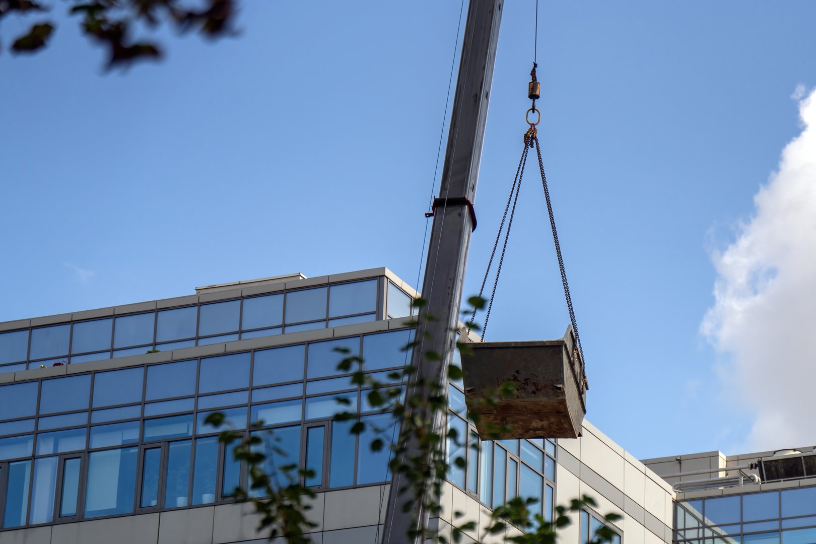 crane hoists an empty metal dumpster above a construction site, symbolizing progress and the cycle of waste management in urban development