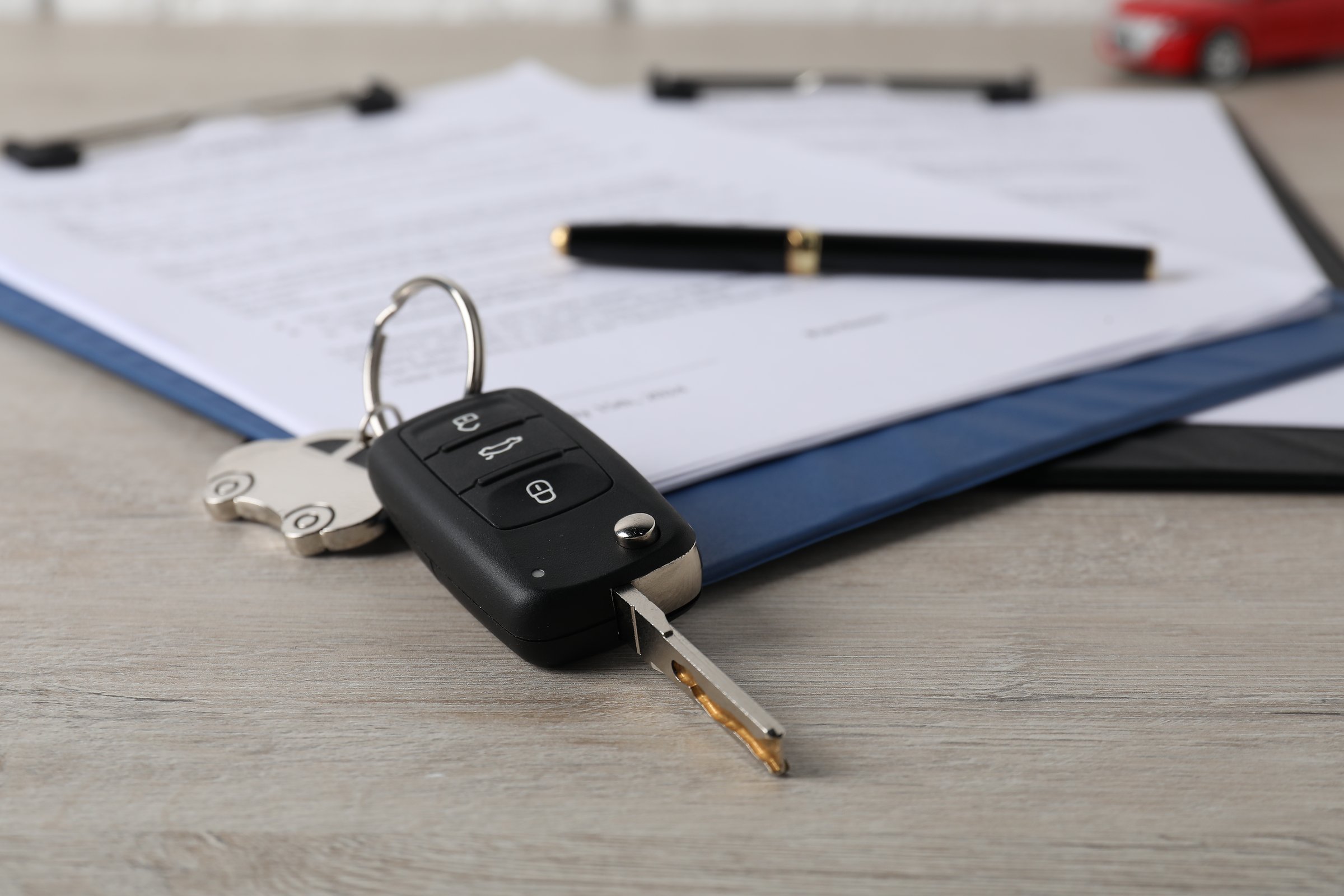 Car key and purchase agreement on wooden table, closeup. Buying auto