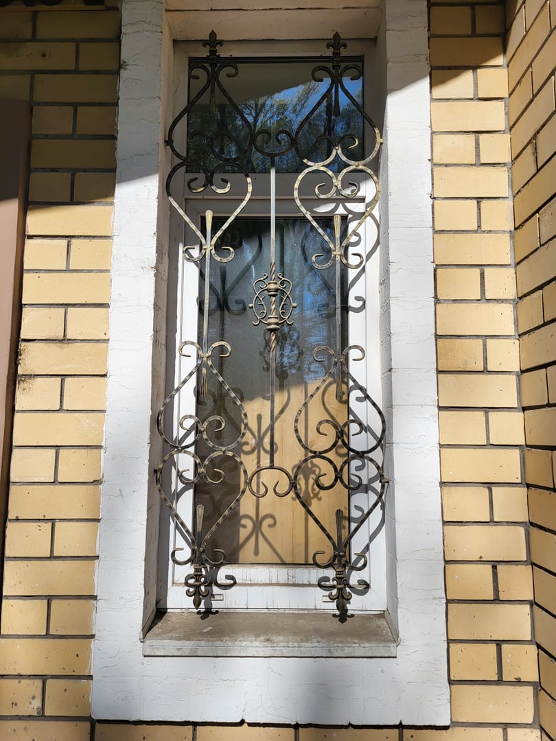 In a sunny spring facade with a narrow window with a wrought-iron grate