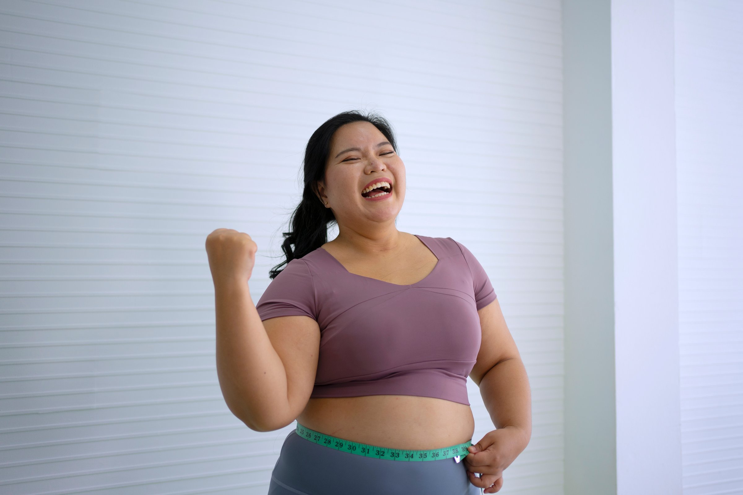 Plus size woman is measure her waist after exercise. Health care and lifestyle concept.