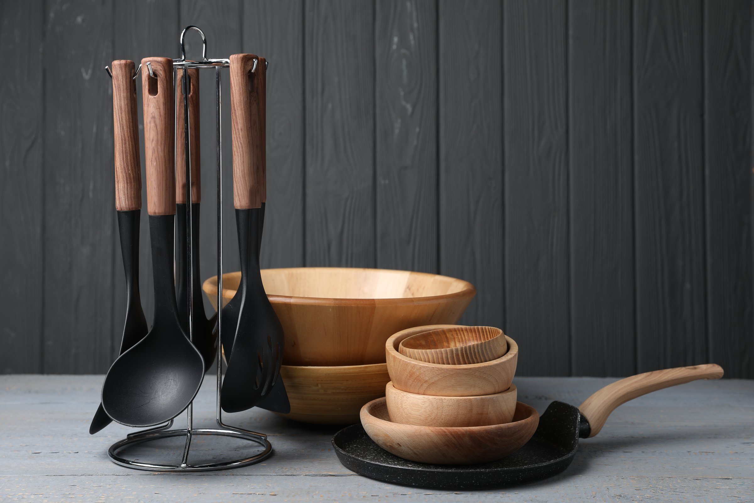 Dishware and cooking utensils on grey wooden table. Space for text