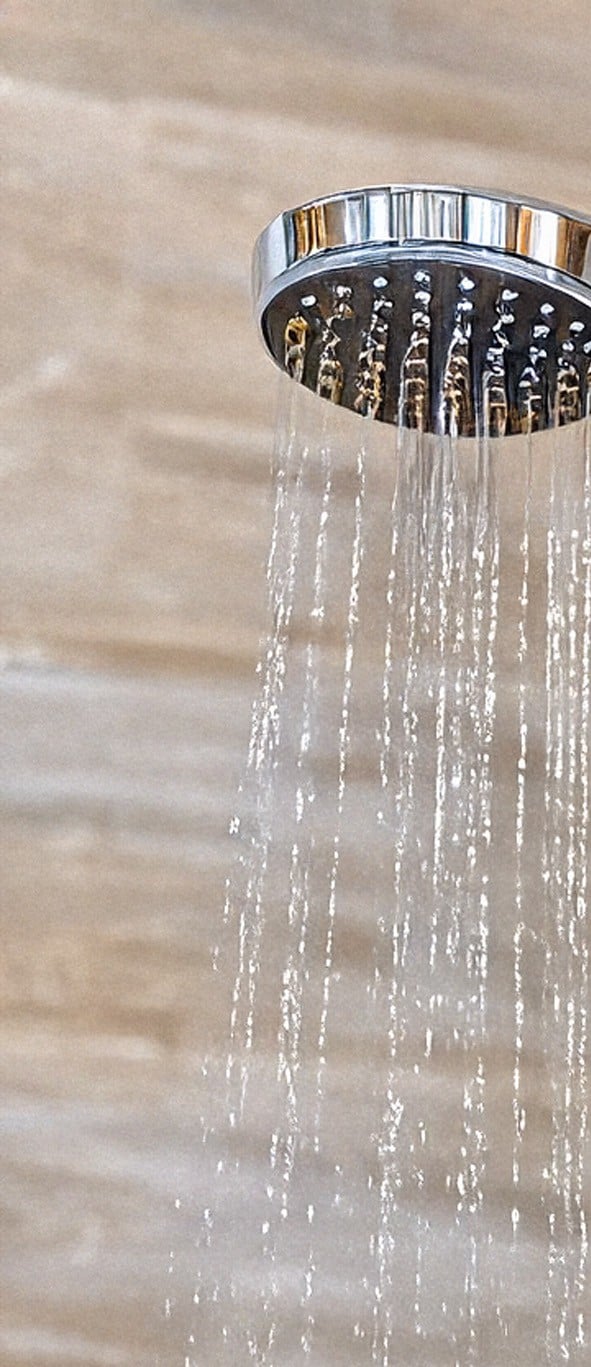 Water flowing from a chrome showerhead against a blurred beige background.