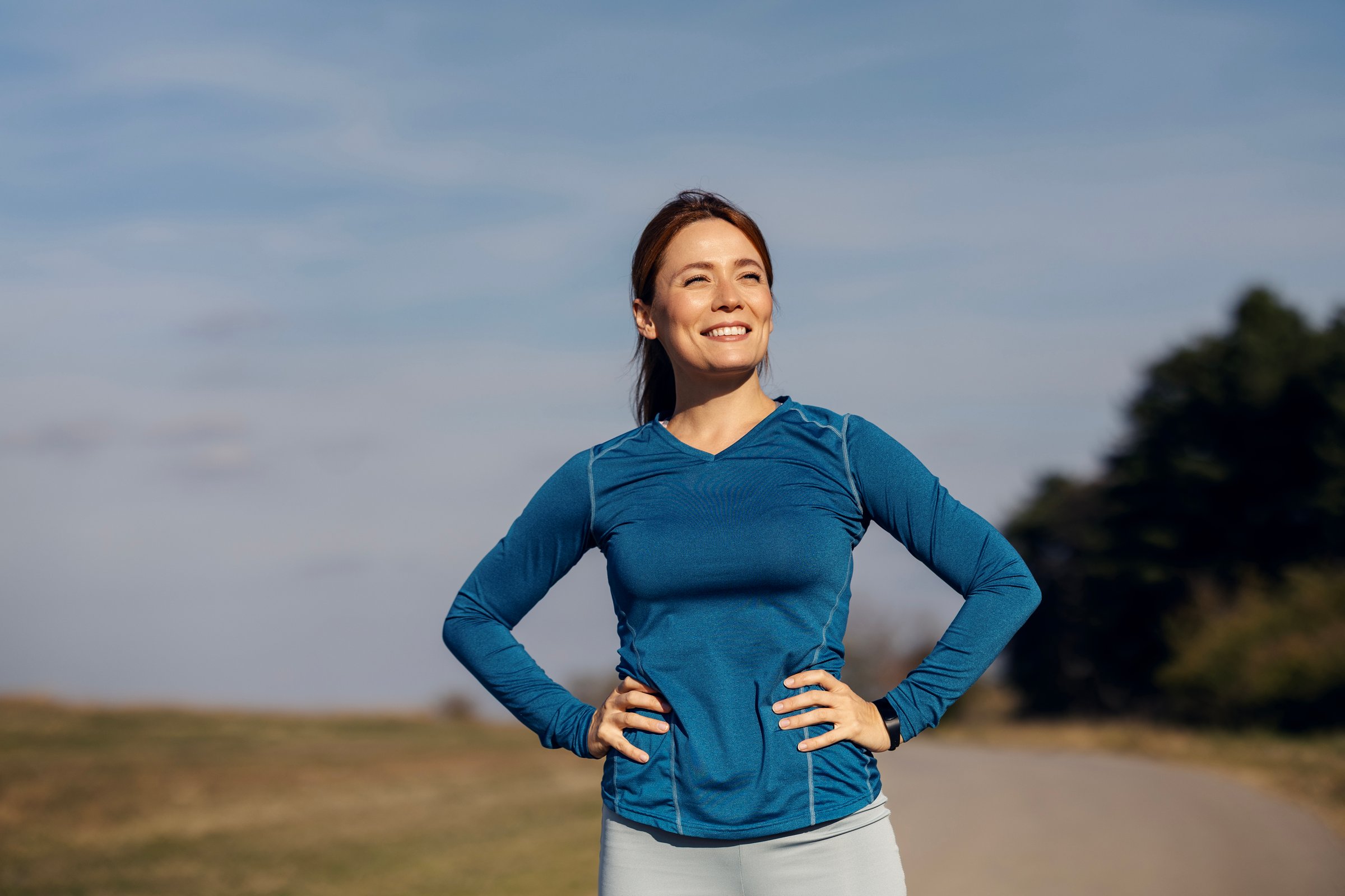 Woman standing with hands on hips, smiling after exercising outdoors