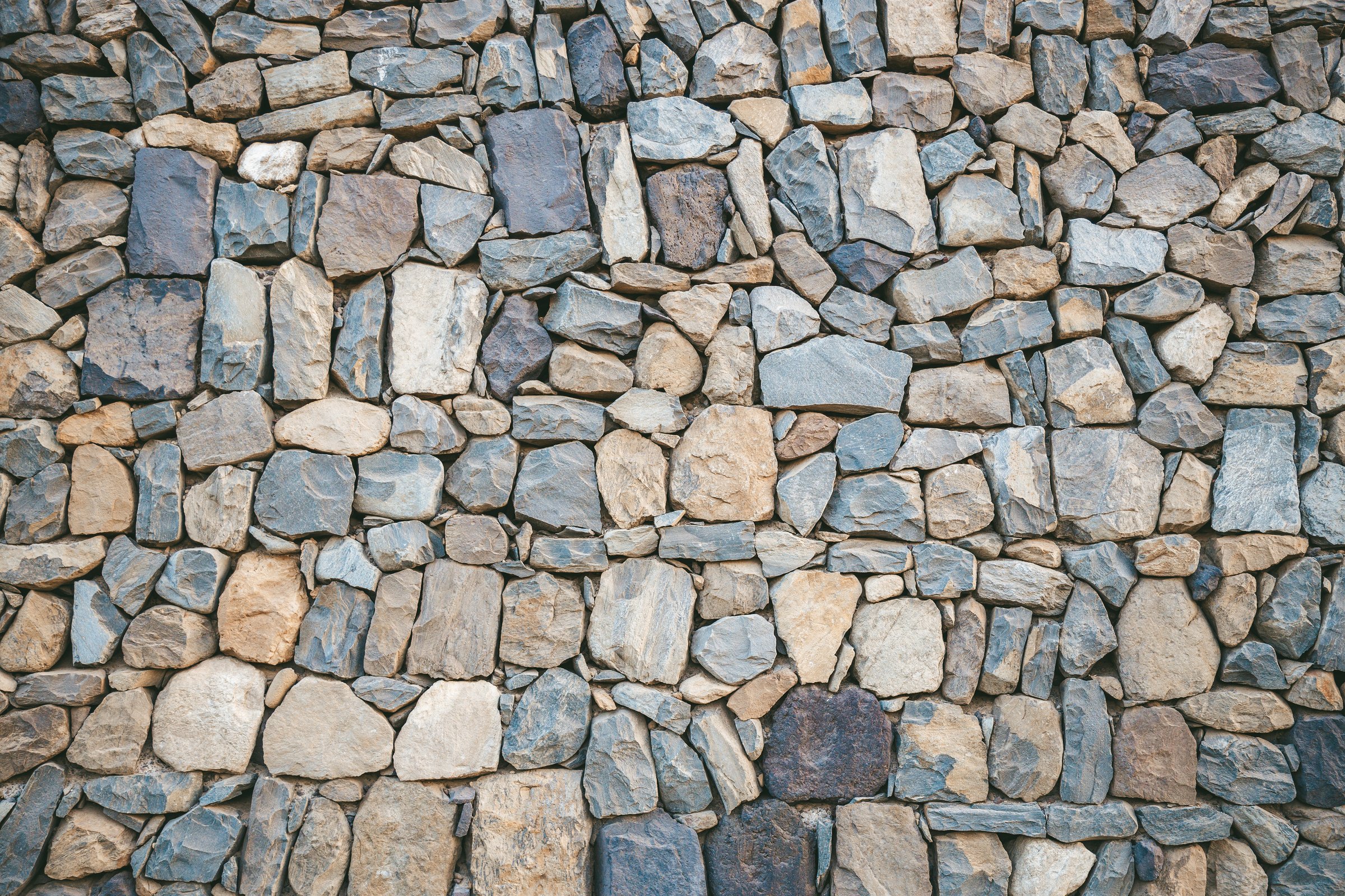 Rustic stone wall showcasing a mix of variously sized stones in natural hues. Ideal for background use, architectural design inspiration, or construction material theme.