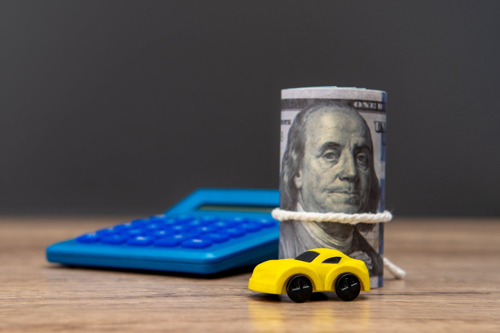 A roll of US dollar bills, a toy car, and a calculator