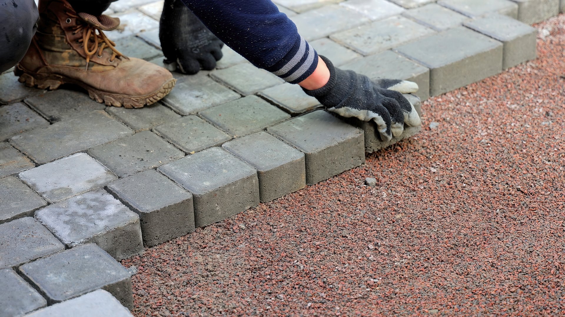 Worker Laying Concrete Pavers on Gravel. Close-up of a worker aligning concrete pavers on compacted gravel
