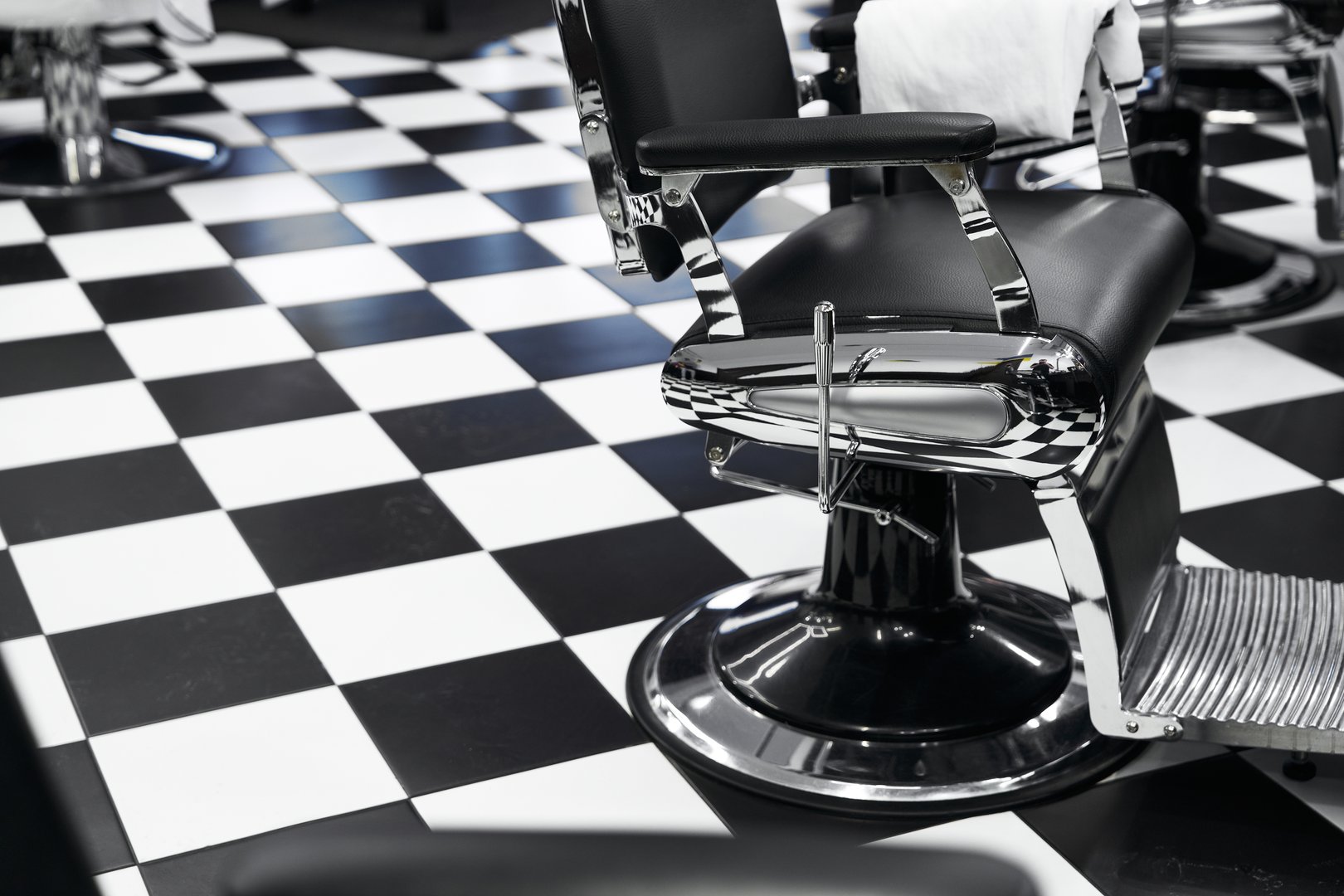 Spacious barbershop features black and white checkerboard flooring with modern styling chairs.