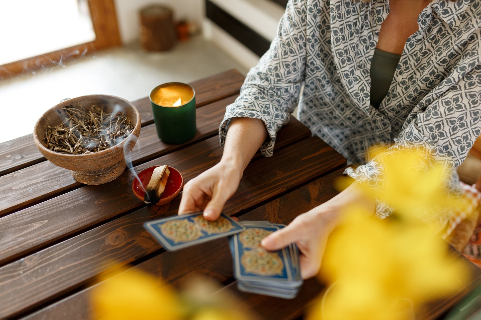 Fortune teller with tarot cards on table near burning candle.Tarot cards spread on table with magic herbs and palo santo aroma sticks. Forecasting concept