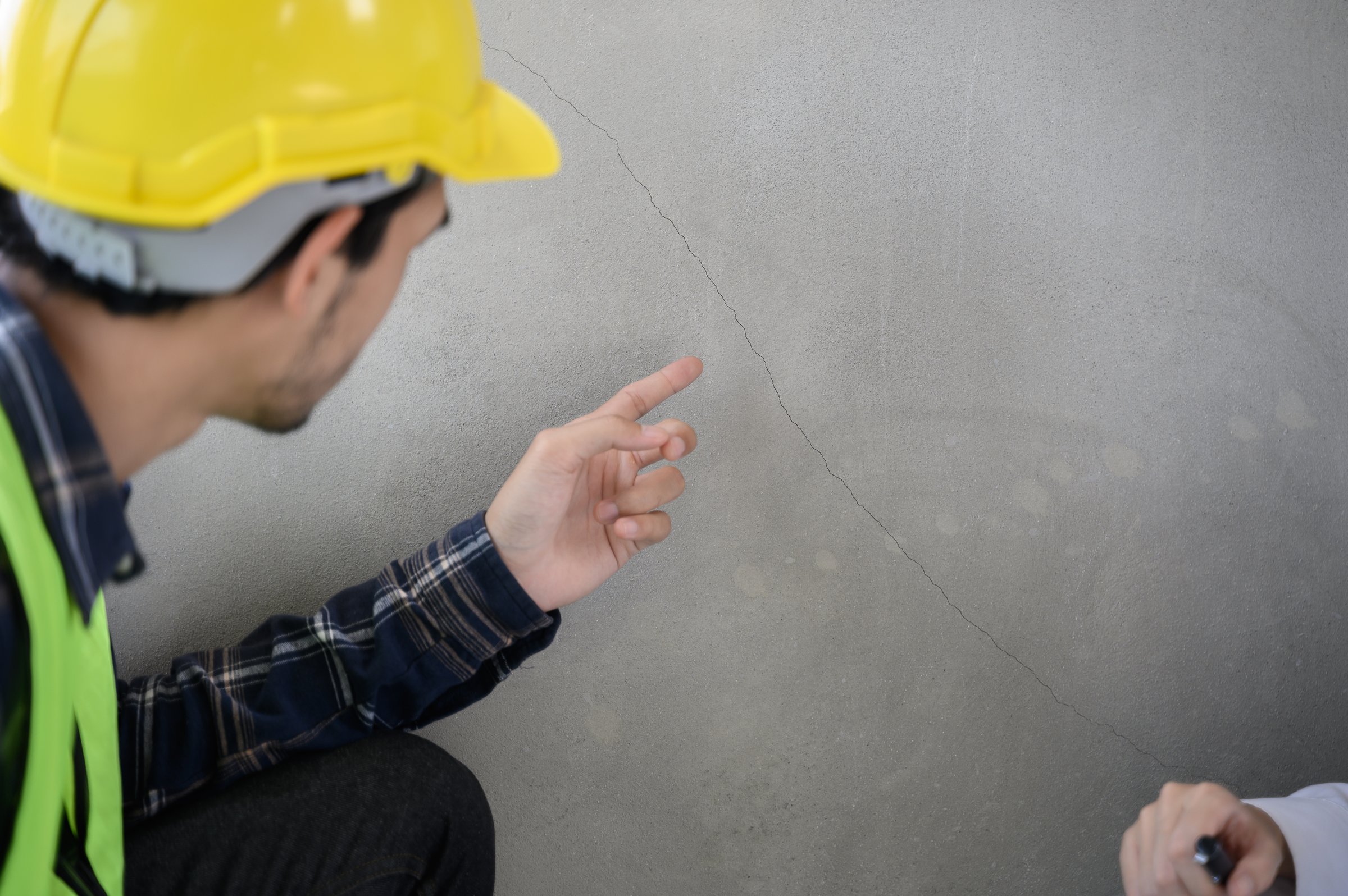 Male civil engineer with inspection check sheet consult with construction site foreman technician for inspect building condition defect pointing wall crack wait for repair.