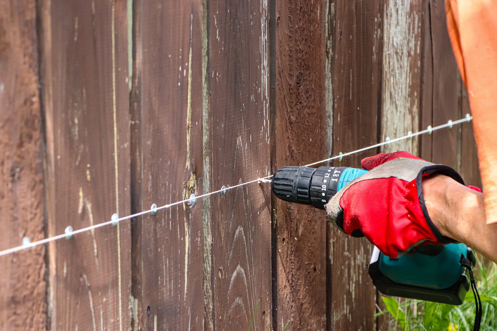A carpenter repairs a wooden fence. Close-up of a working tool. A screwdriver in the hand of a master. Carpenter in red gloves. Safe tool. Screws and screws are screwed into a wooden fence
