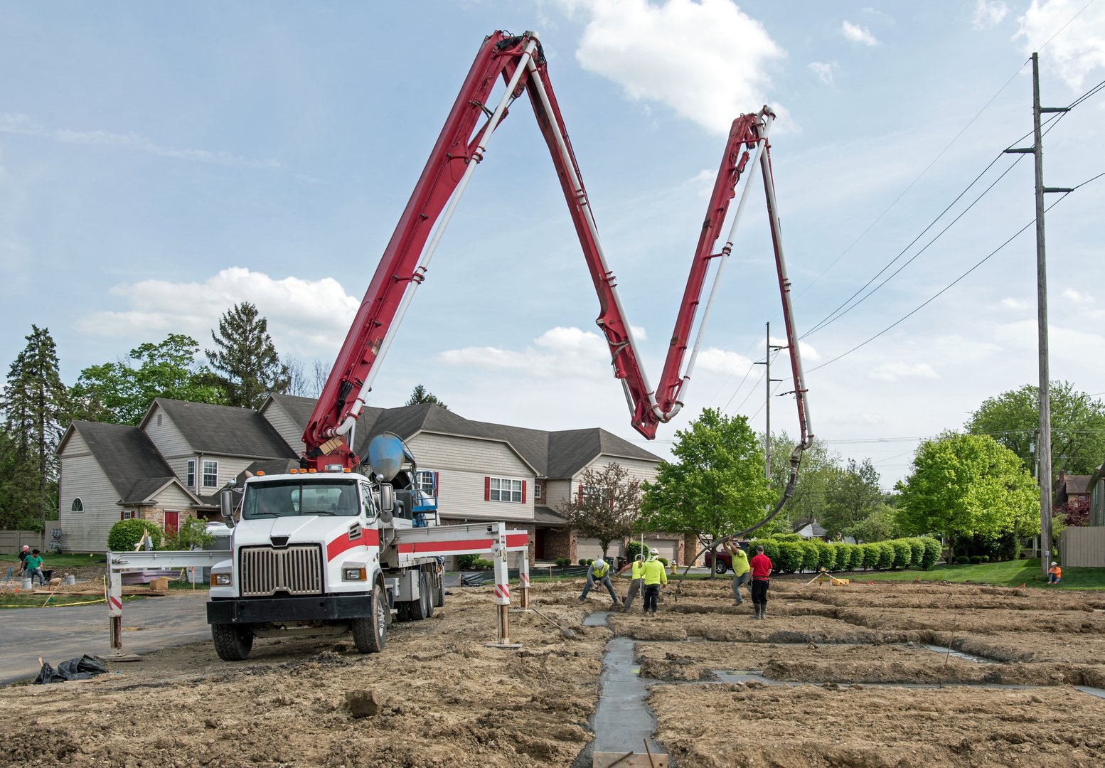 Dayton, Ohio - May 1, 2024: Construction worker directs concrete flowing from boom pump through flexible hose into footer while others work the concrete smooth.