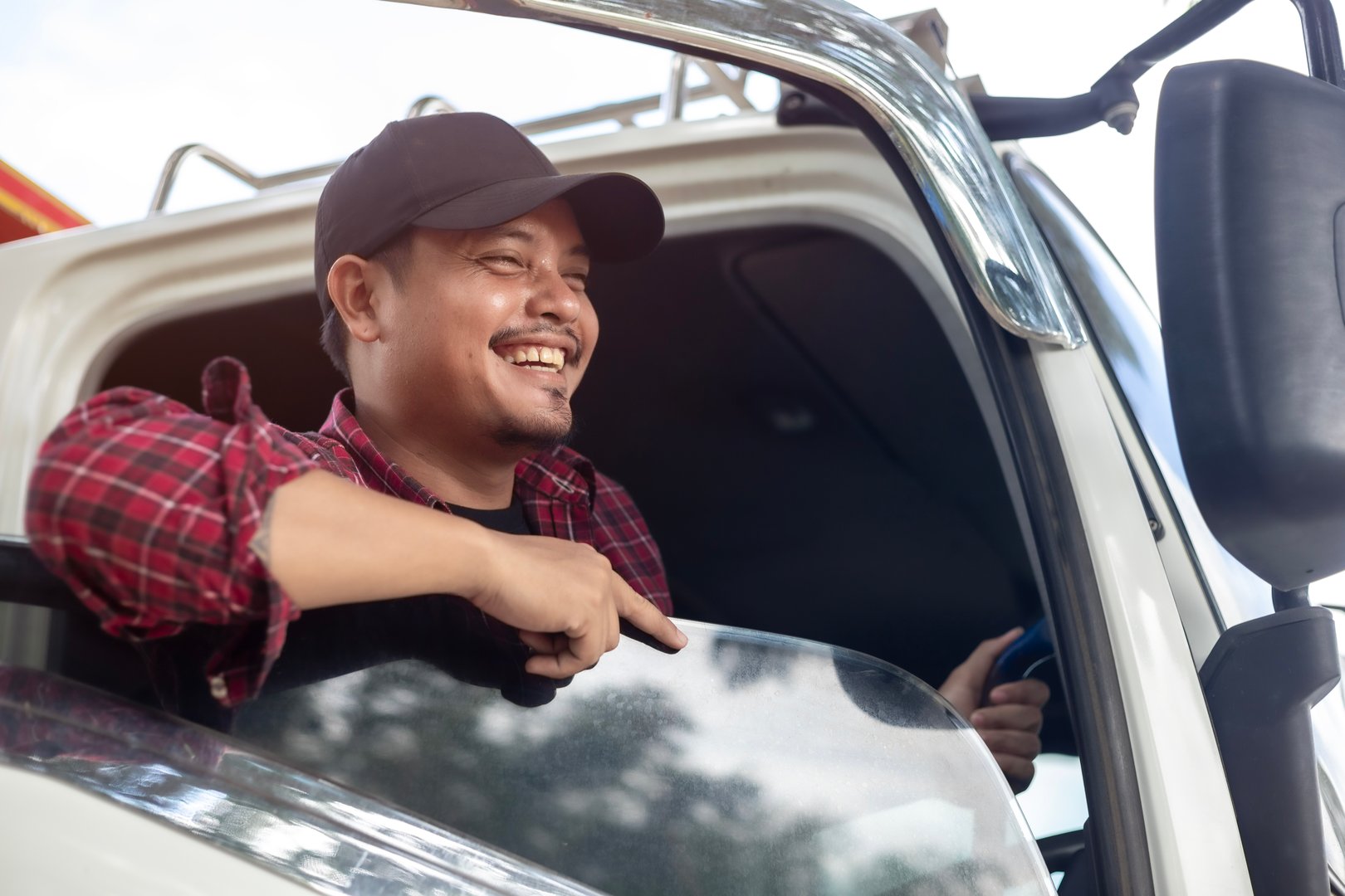 A man in a truck is smiling and pointing out the window. Scene is happy and lighthearted