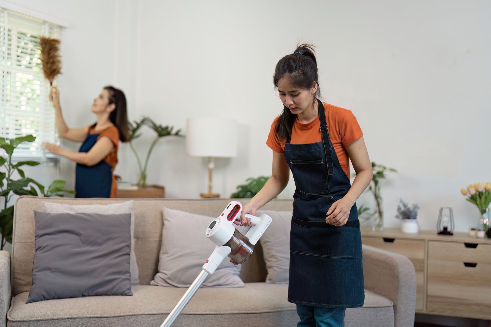 A woman cleans a living room using a vacuum and duster, showcasing a tidy and organized modern home environment.