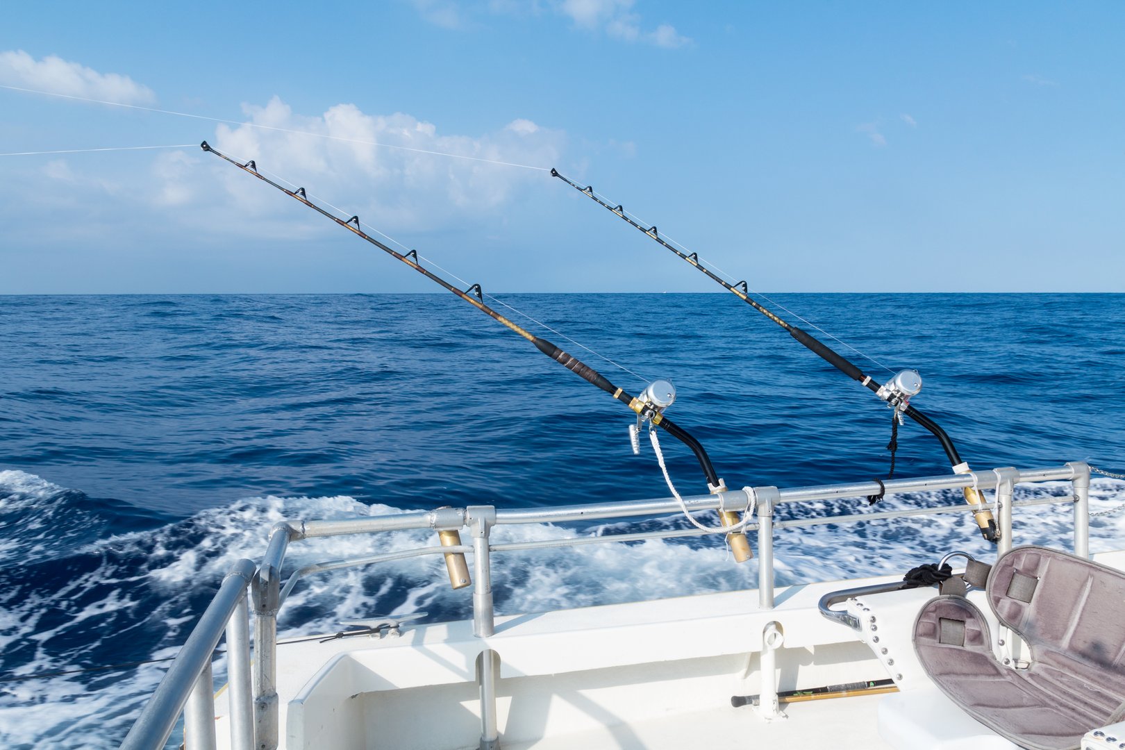 Sport fishing with two salt water rods and reels. Deep sea fishing in the ocean on a sunny blue sky day with fluffy clouds.