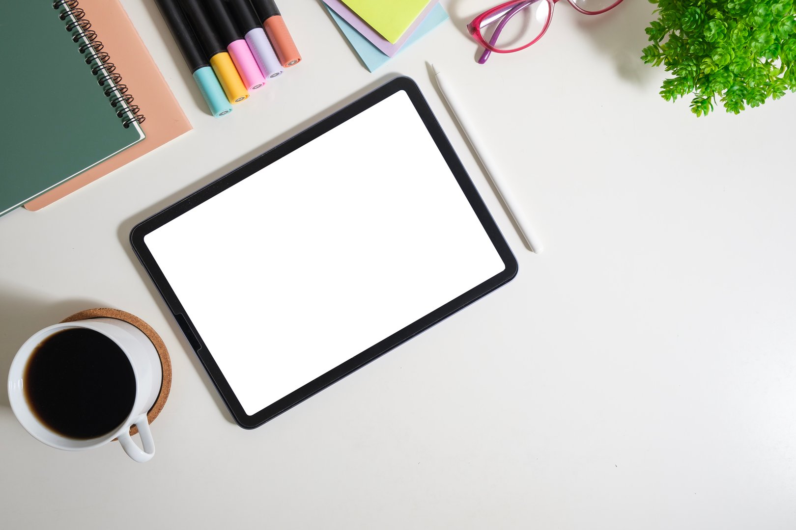 Digital tablet with blank screen, glasses, coffee cup and stationery on white table. Flat lay, top view with copy space.