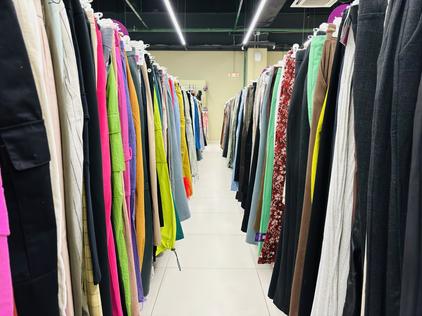 Clothing pants on hangers, on rails in a second-hand store. Colored clothes display in market. Huge selection of different used clothes for men, women and children on the rack in thrift store. Symmetrical photo