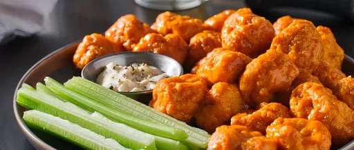 Buffalo cauliflower wings with dipping sauce and celery sticks on a black plate.