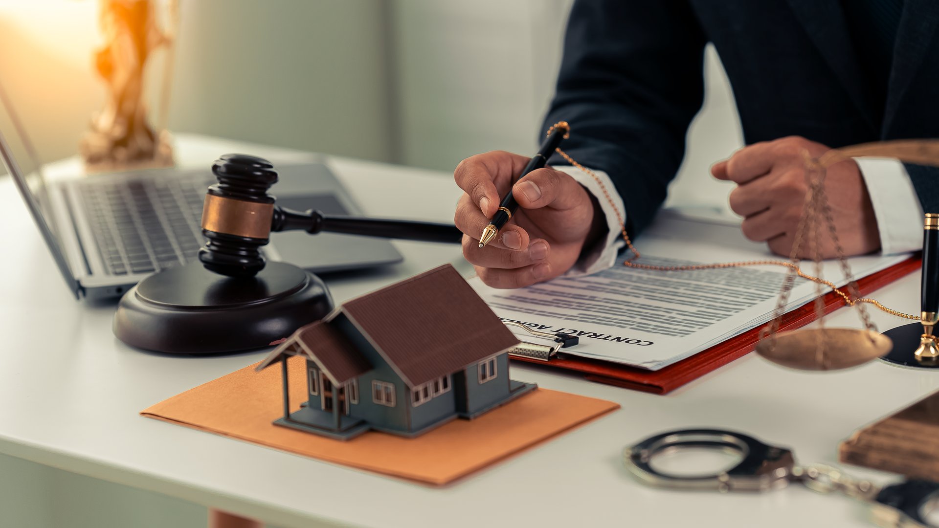 Close-up of lawyer sitting at desk with scale, hammer and small wooden toy house, working with documents, signing contracts, real estate law, foreclosed property that cannot be paid off.