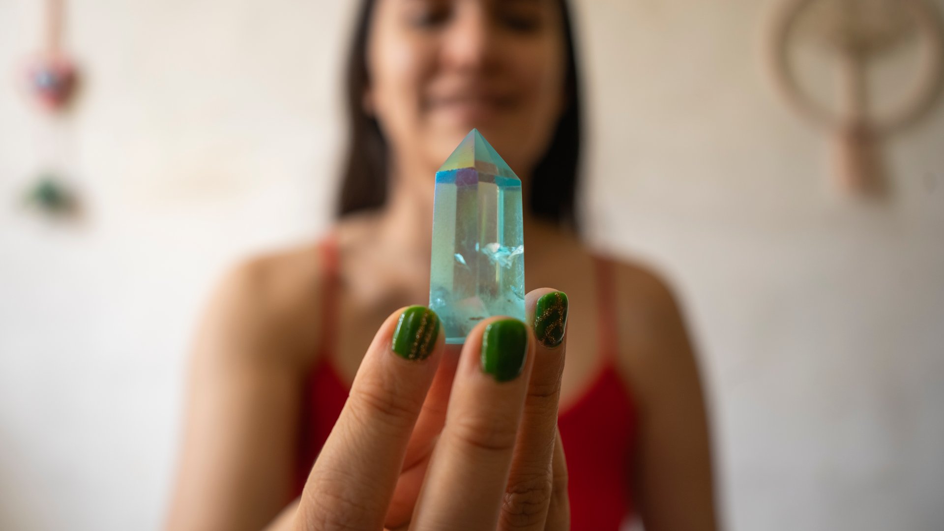 Young woman holding a clear aqua blue aura quartz crystal point, surrounded by a softly blurred background and decorative elements, radiating energy and a sense of spirituality
