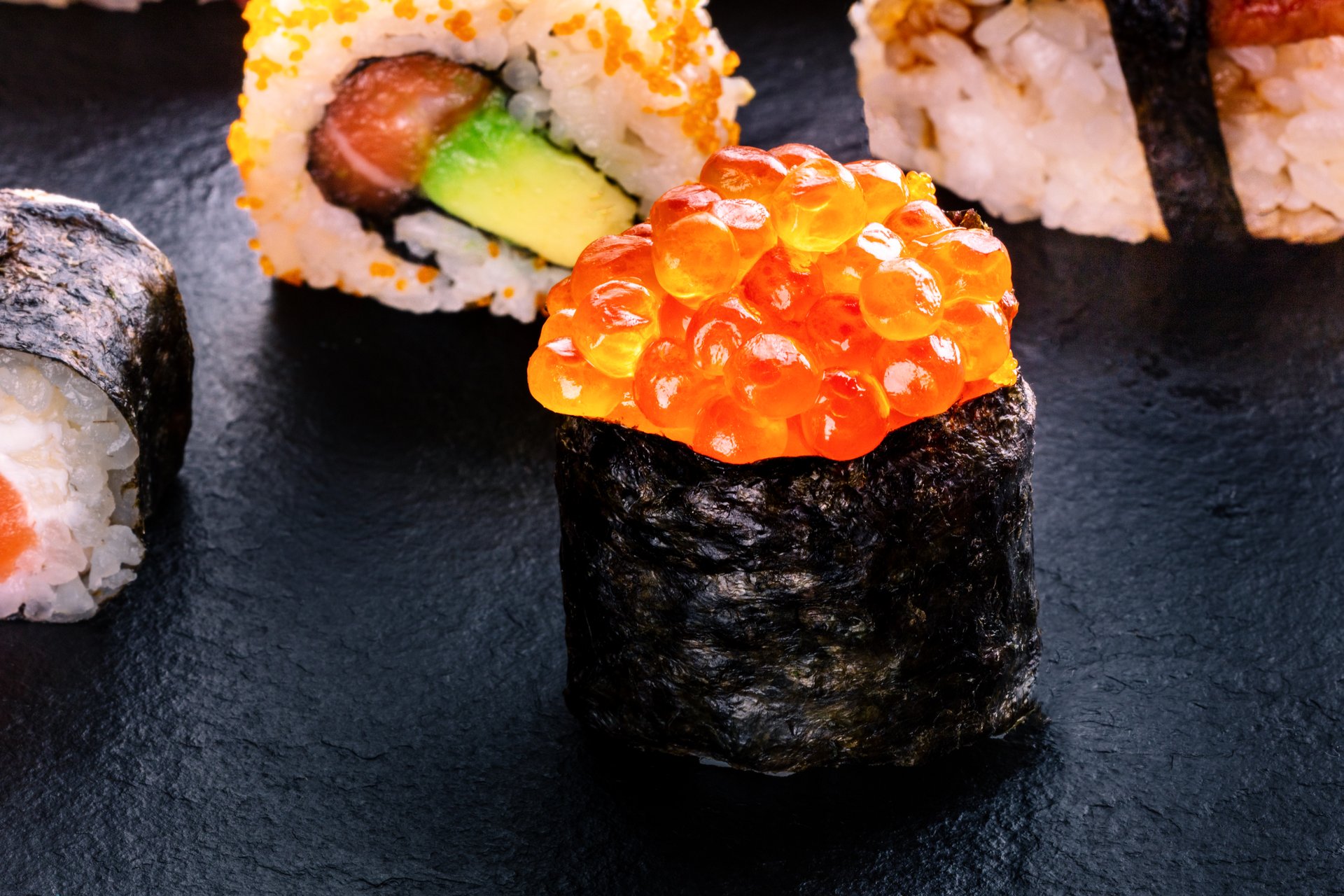 Sushi rolls on a black background. Ikura maki roll and others on a black slate background