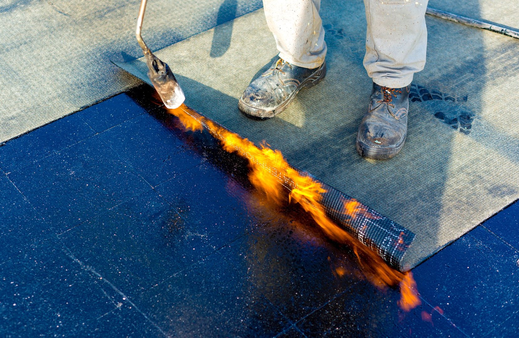 Worker preparing part of bitumen roofing felt roll for melting by gas heater torch flame
